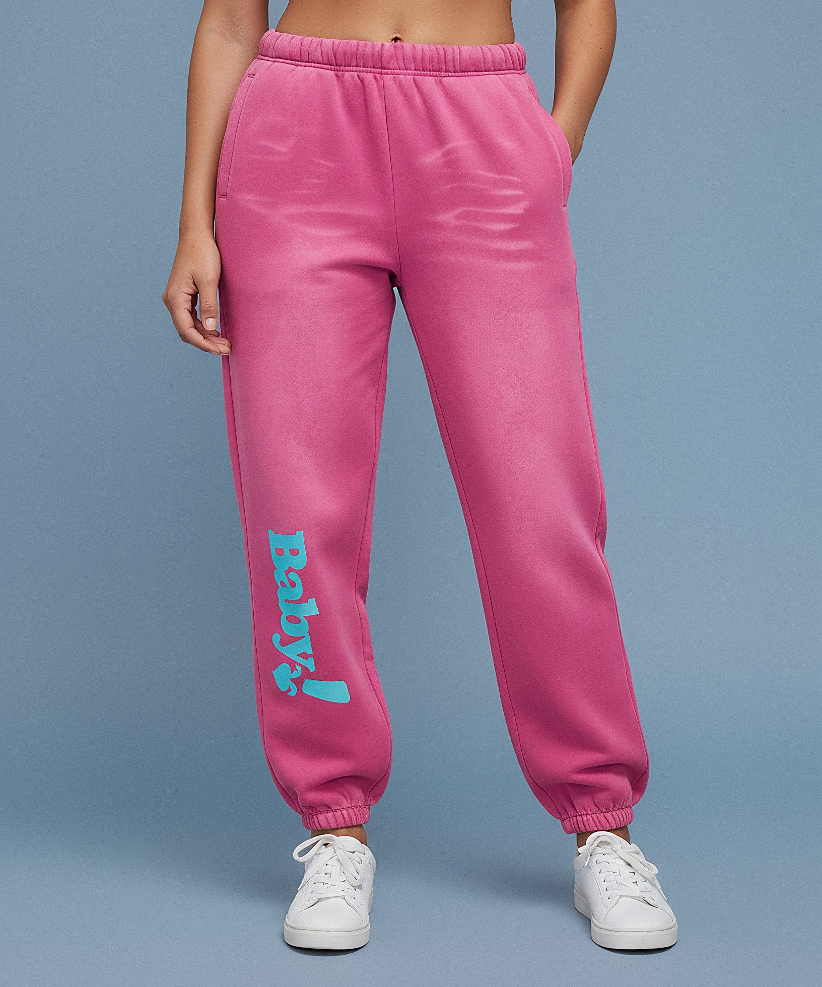 Pink sweatpants with sweethearts  'Baby!' text on a blue background, female front view