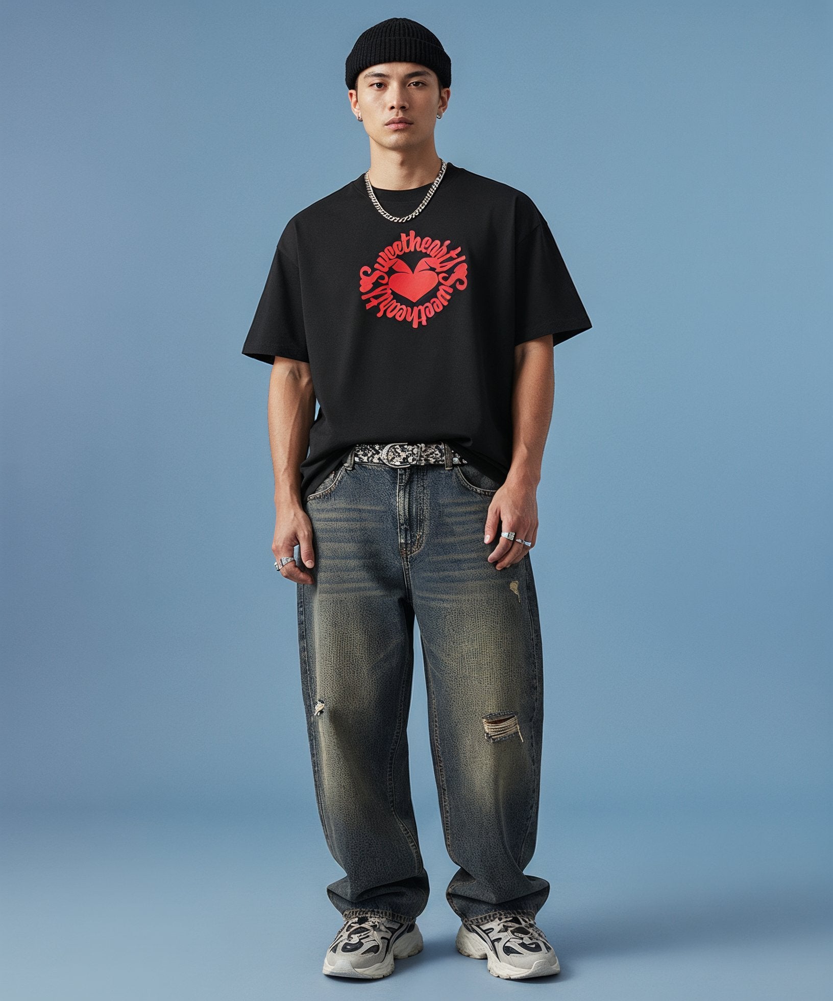 male wearing a black t-shirt with sweethearts red heart logo graphics and text in a circle and distressed jeans on a blue background, front view