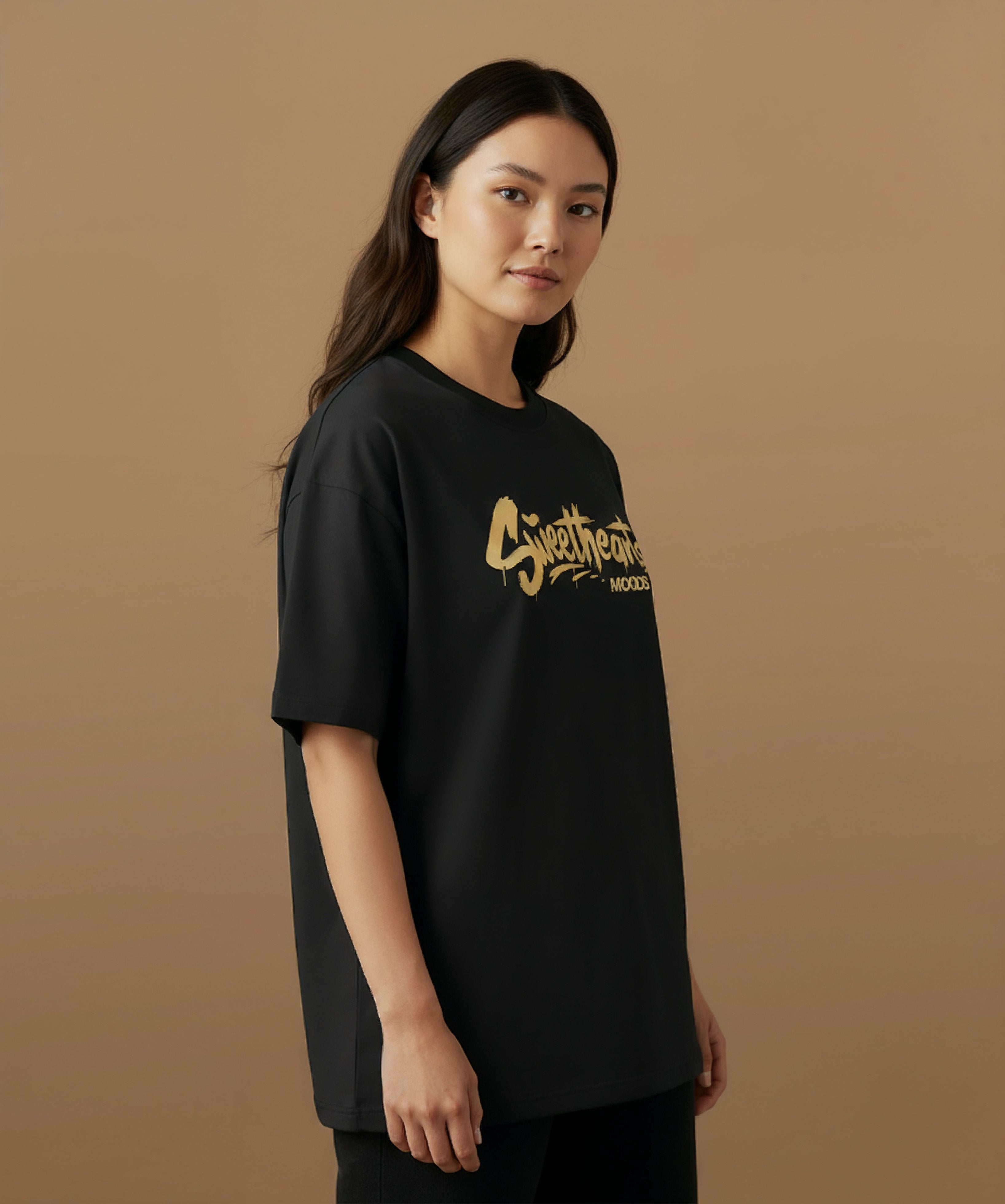 Male model wearing a black t-shirt with 'Sweethearts' logo from moods collection,  graffiti text logo, on a brown background, angled right pose