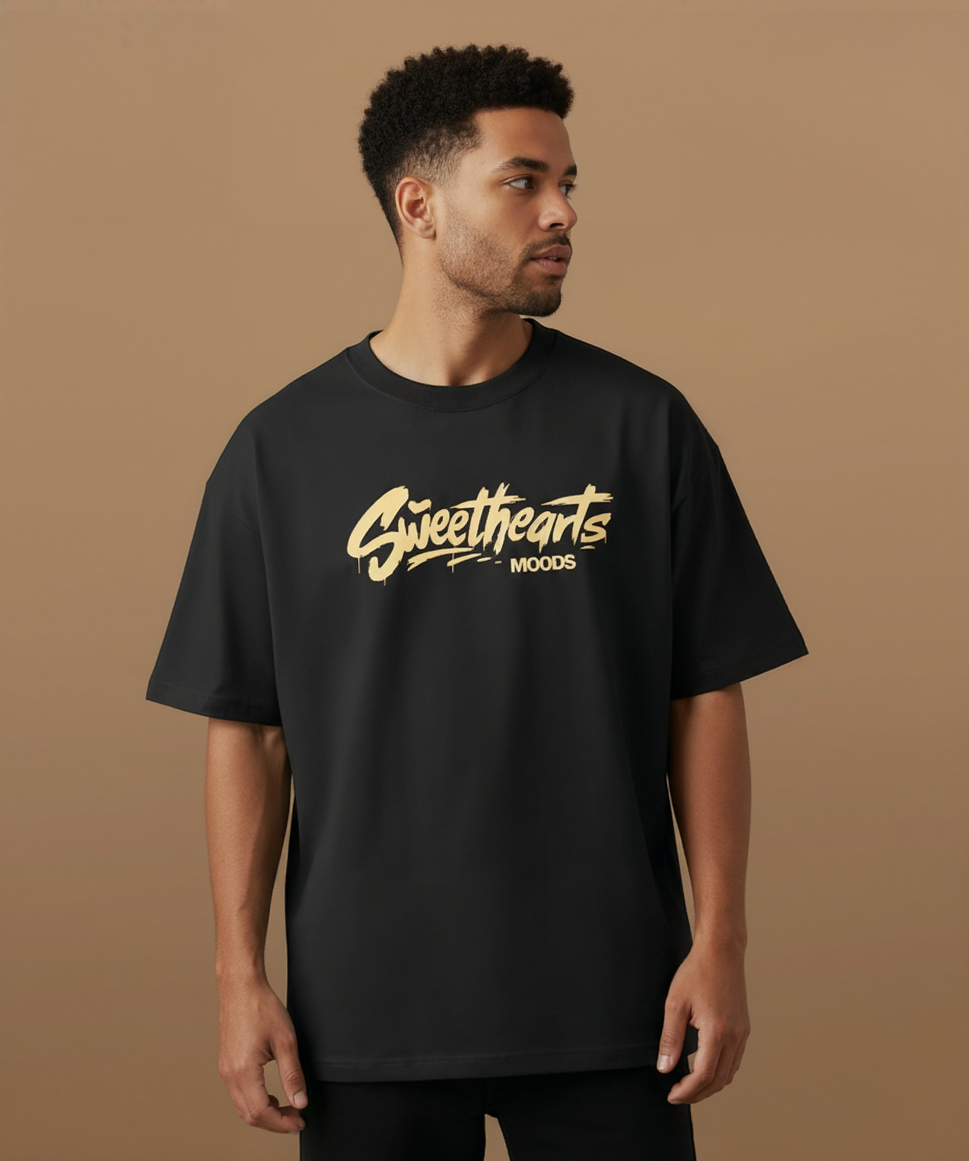 Male model wearing a black t-shirt with 'Sweethearts' logo from moods collection,  graffiti text logo, on a brown background