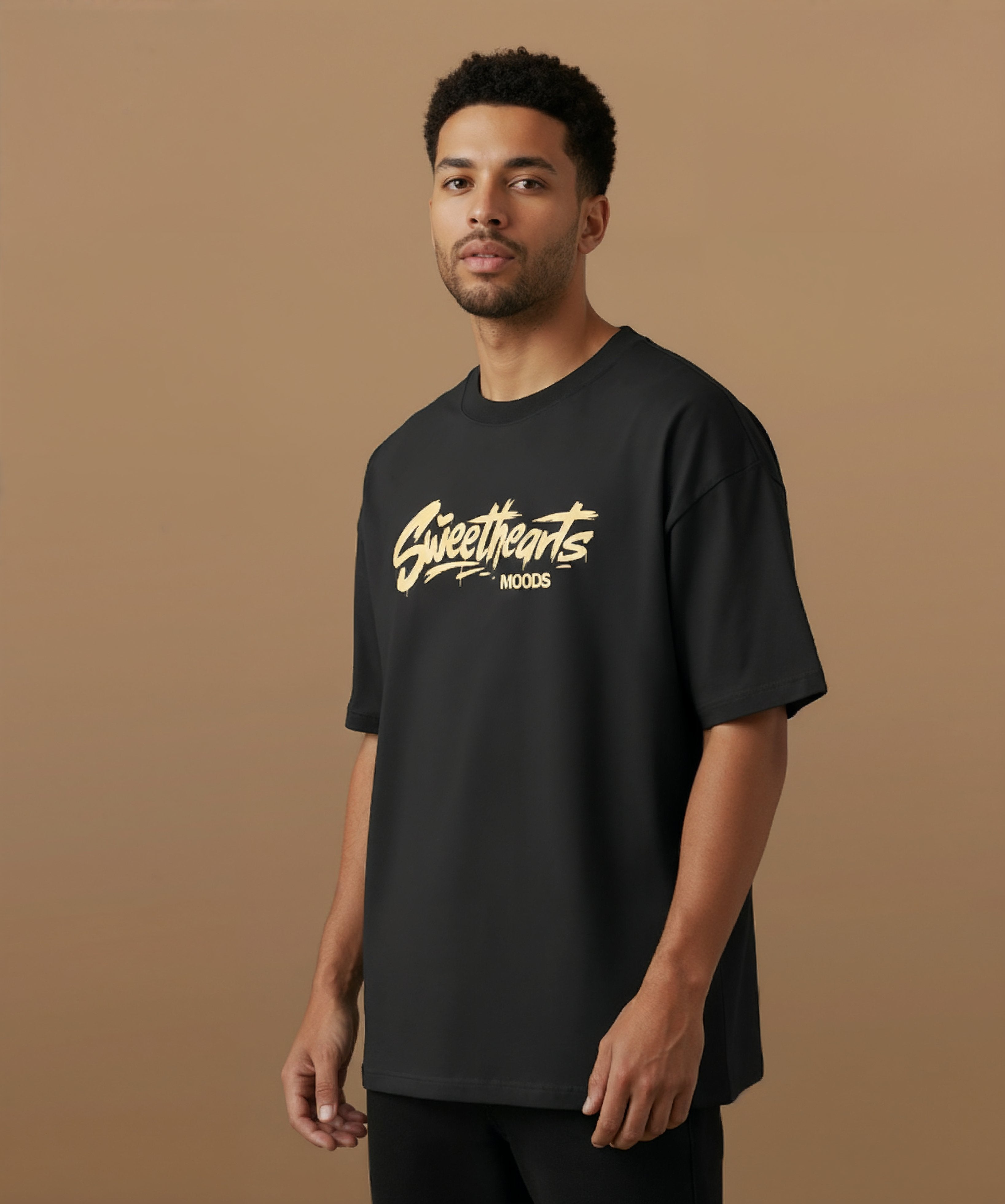 Male model wearing a black t-shirt with 'Sweethearts' logo from moods collection,  graffiti text logo, on a brown background, angled left