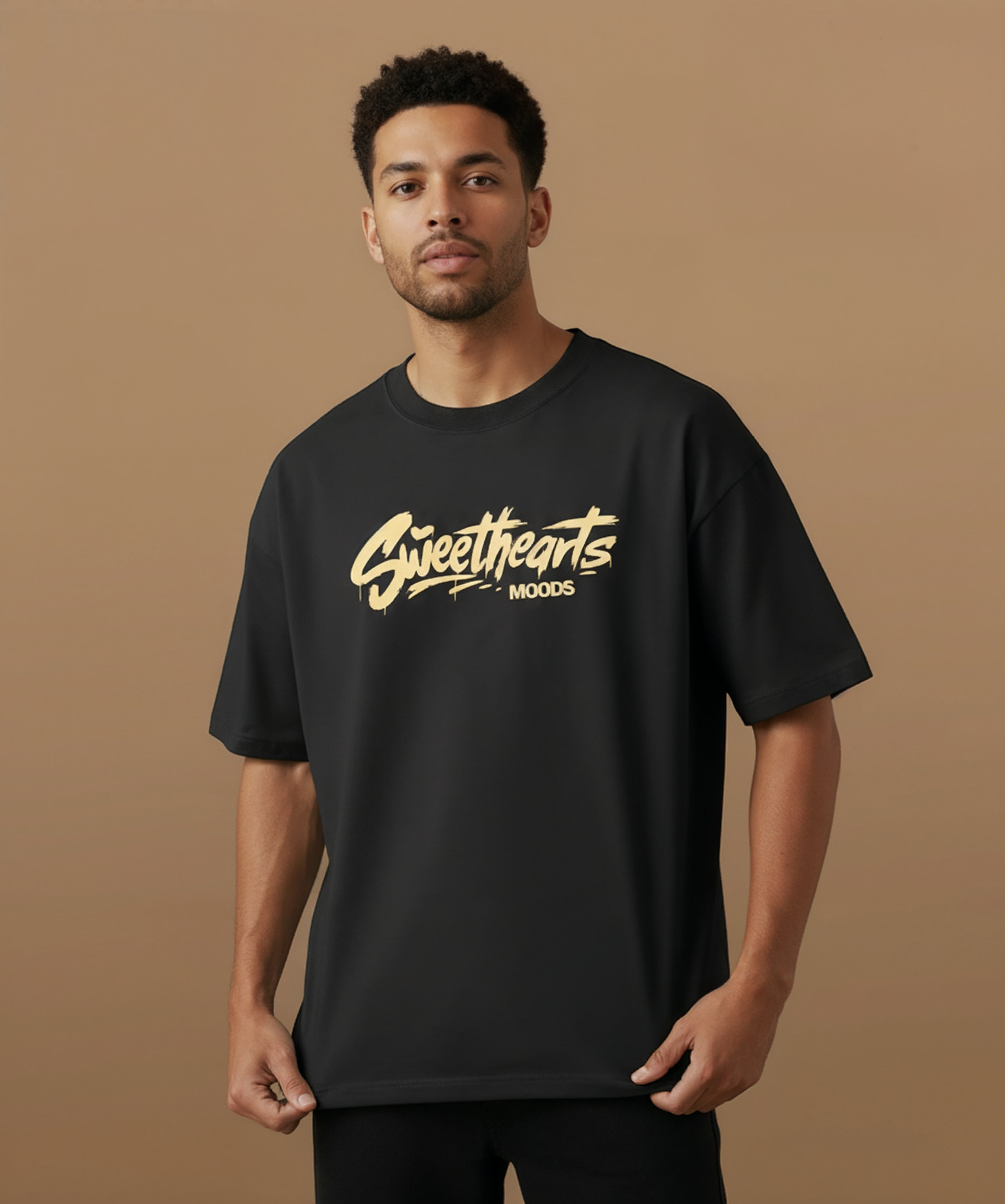Male model wearing a black t-shirt with 'Sweethearts' logo from moods collection,  graffiti text logo, on a brown background, angled center