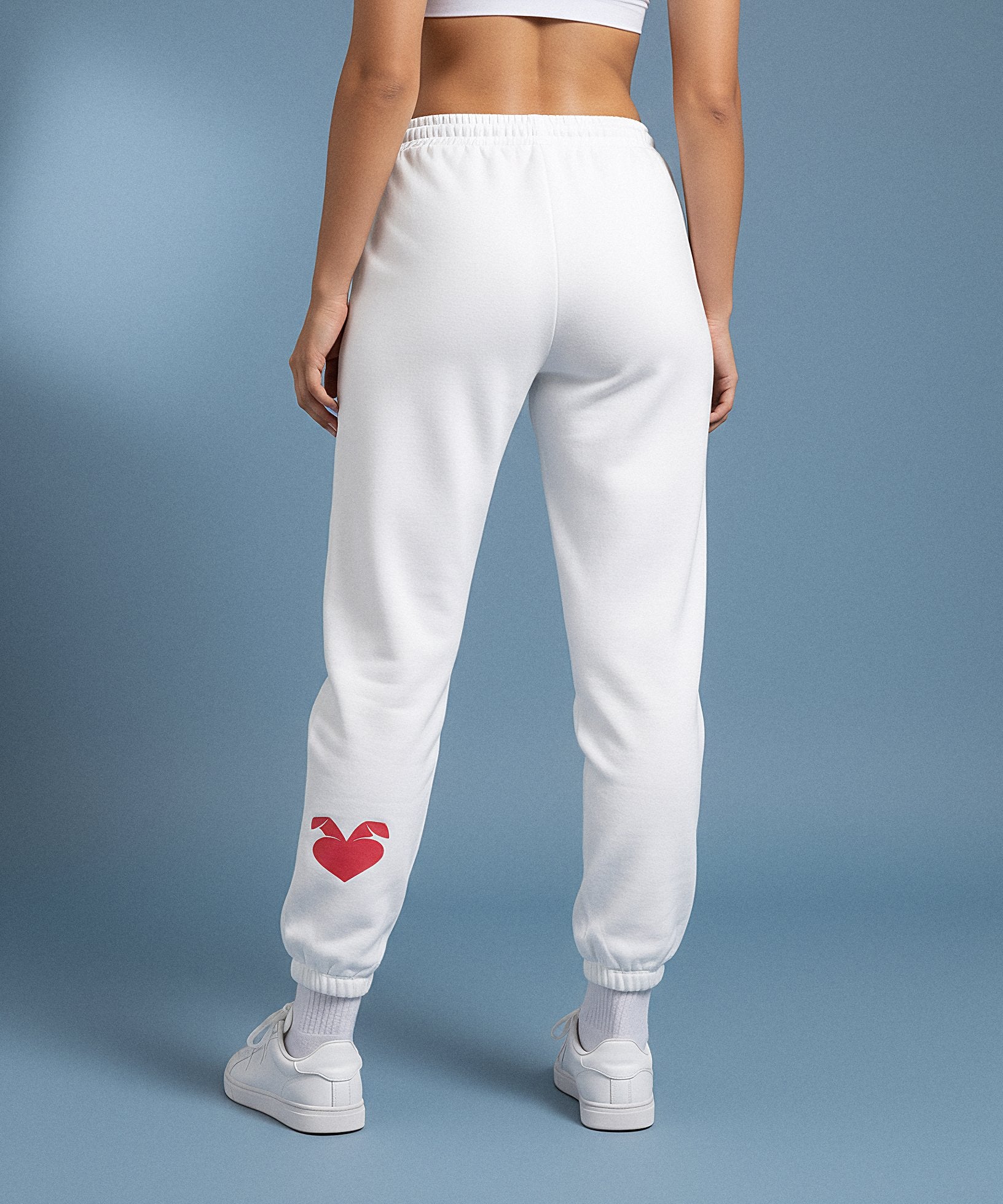 white sweatpants with a red heart design on the back, worn by a person against a blue background. back view