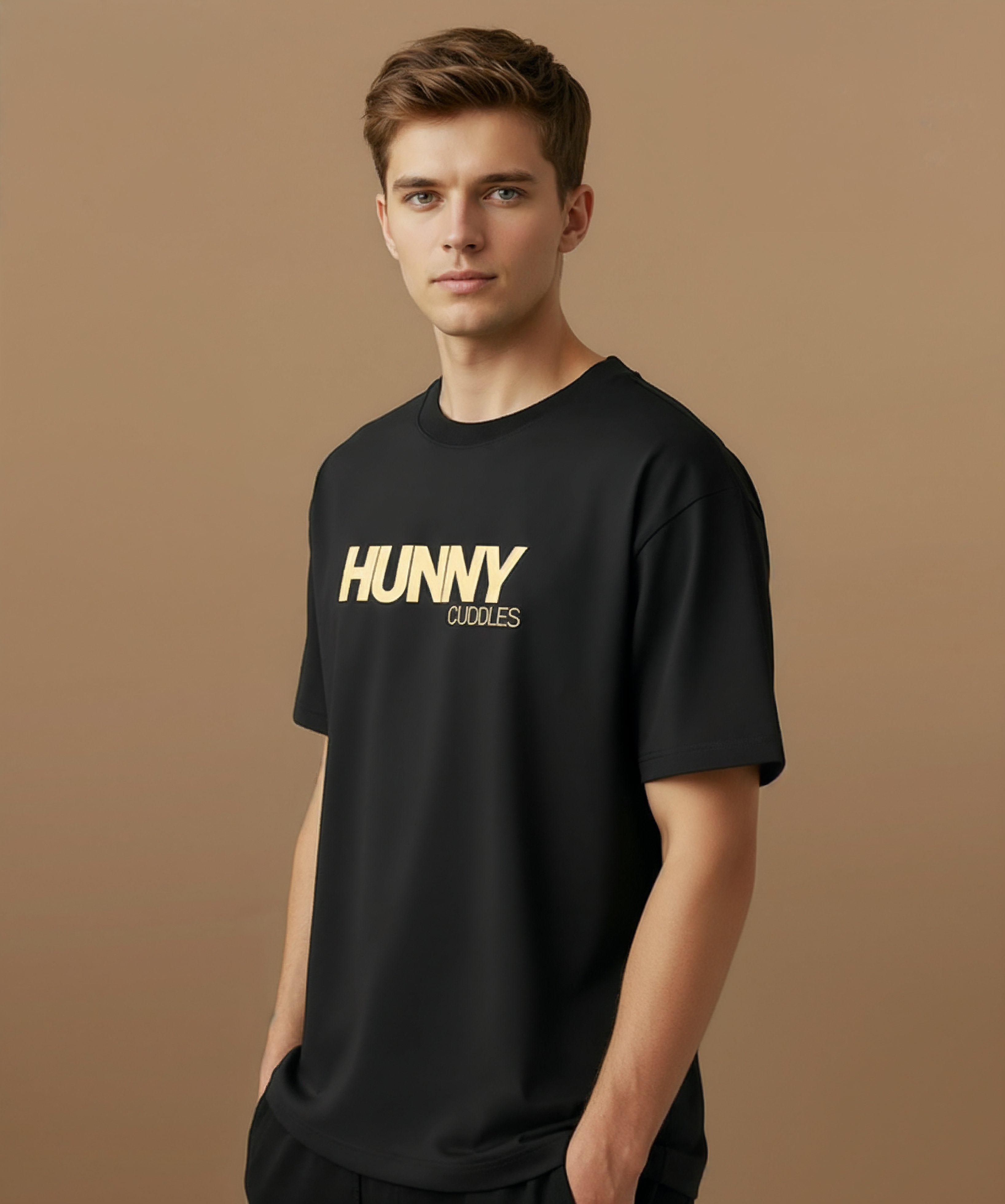 Male model wearing a black t-shirt with 'HUNNY CUDDLES' text on a beige background, angled left