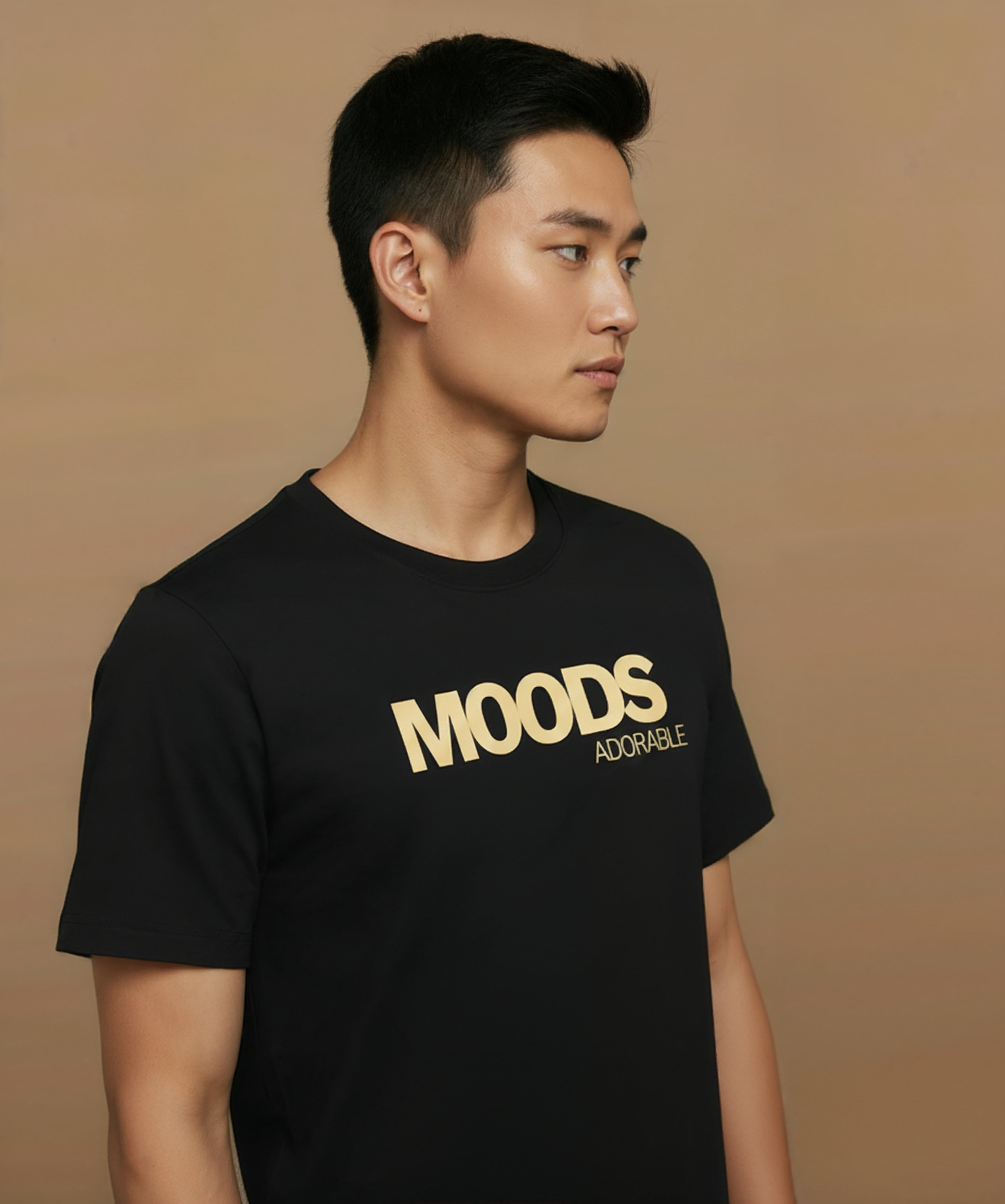 Man wearing a black t-shirt with 'MOODS', adorable, printed in gold on a brown background, angled right