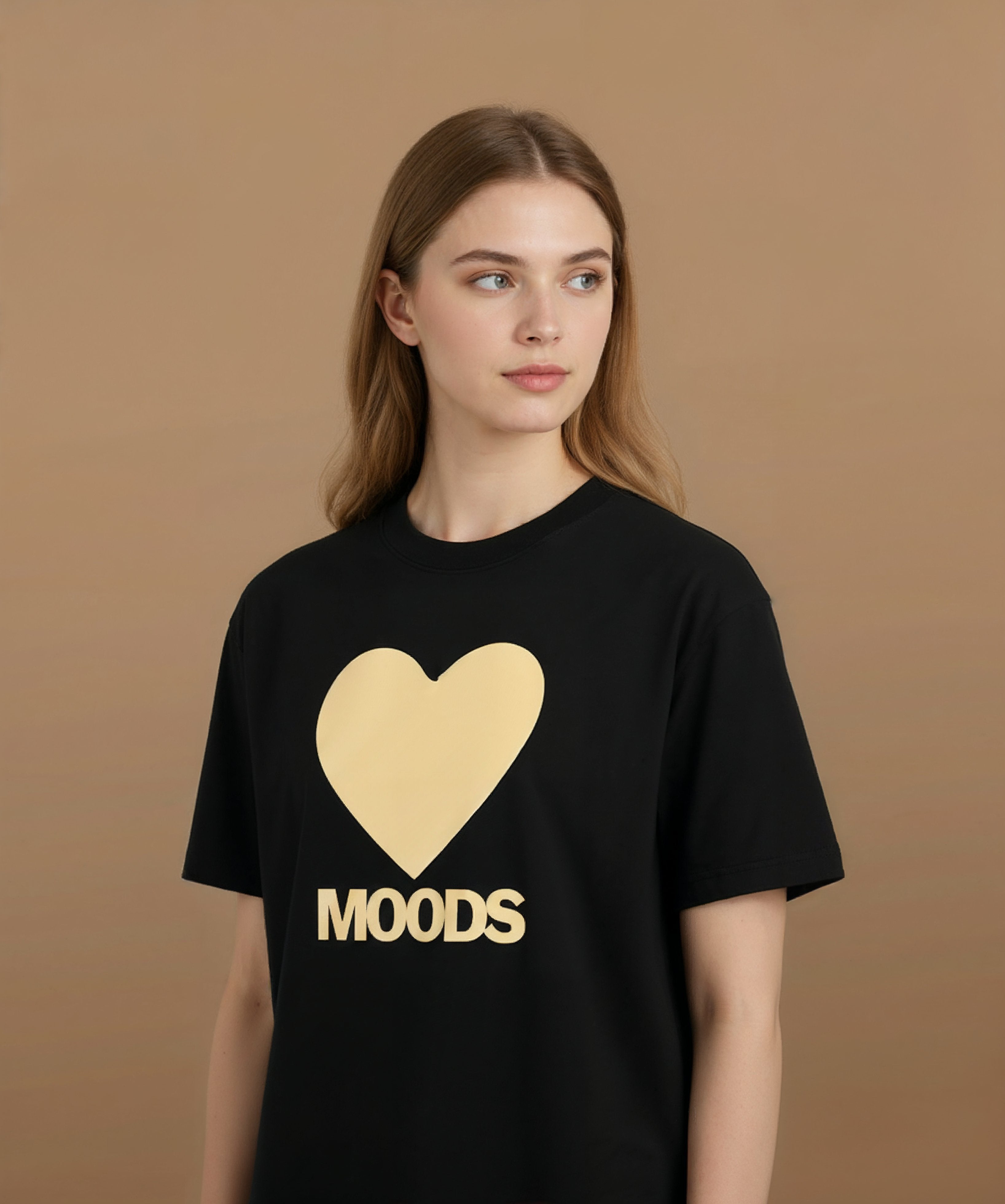 a female wearing a black sweethearts t-shirt with a gold heart and 'MOODS' text on a brown background, angled left