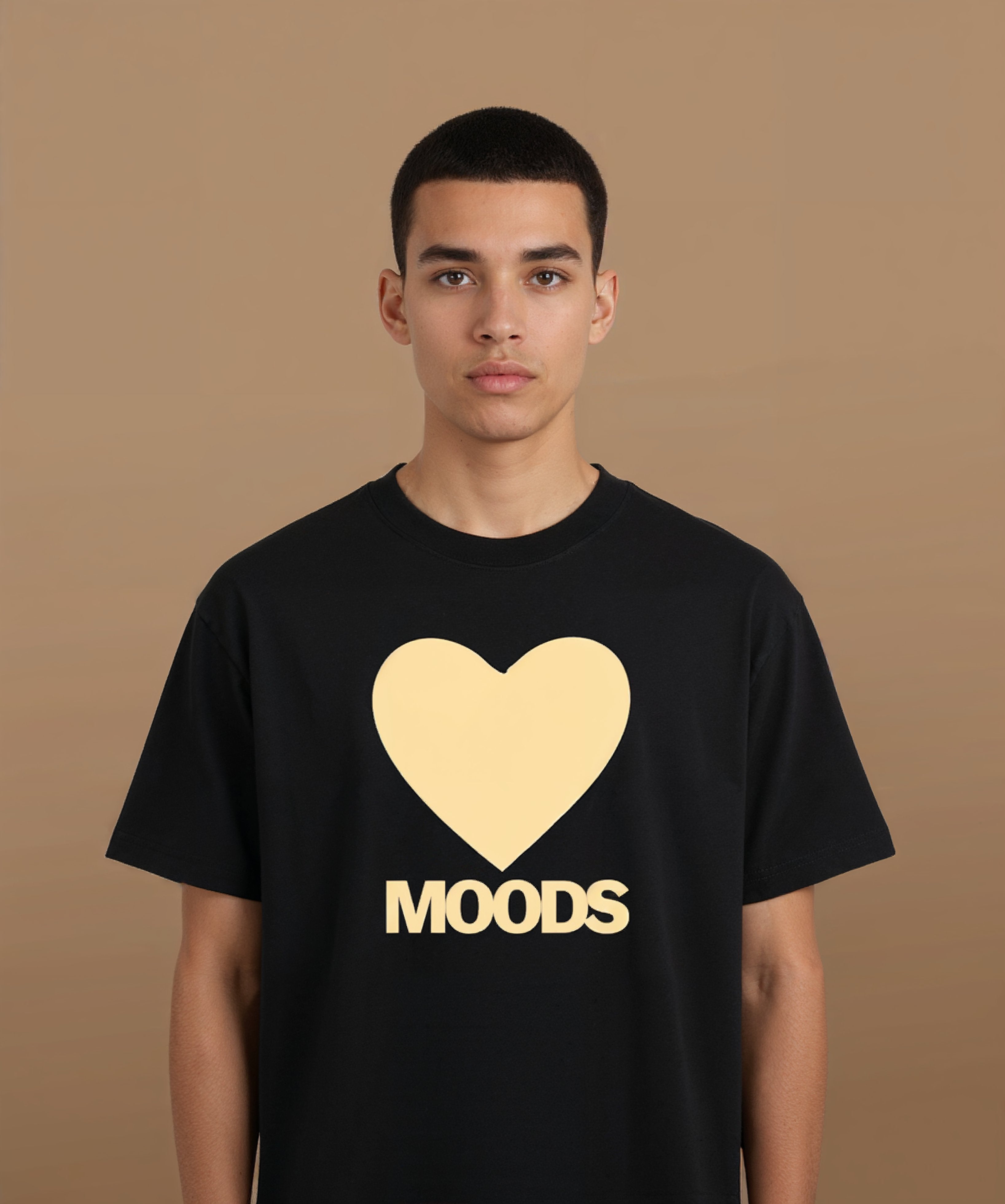 a male wearing a black sweethearts t-shirt with a gold heart and 'MOODS' text on a brown background