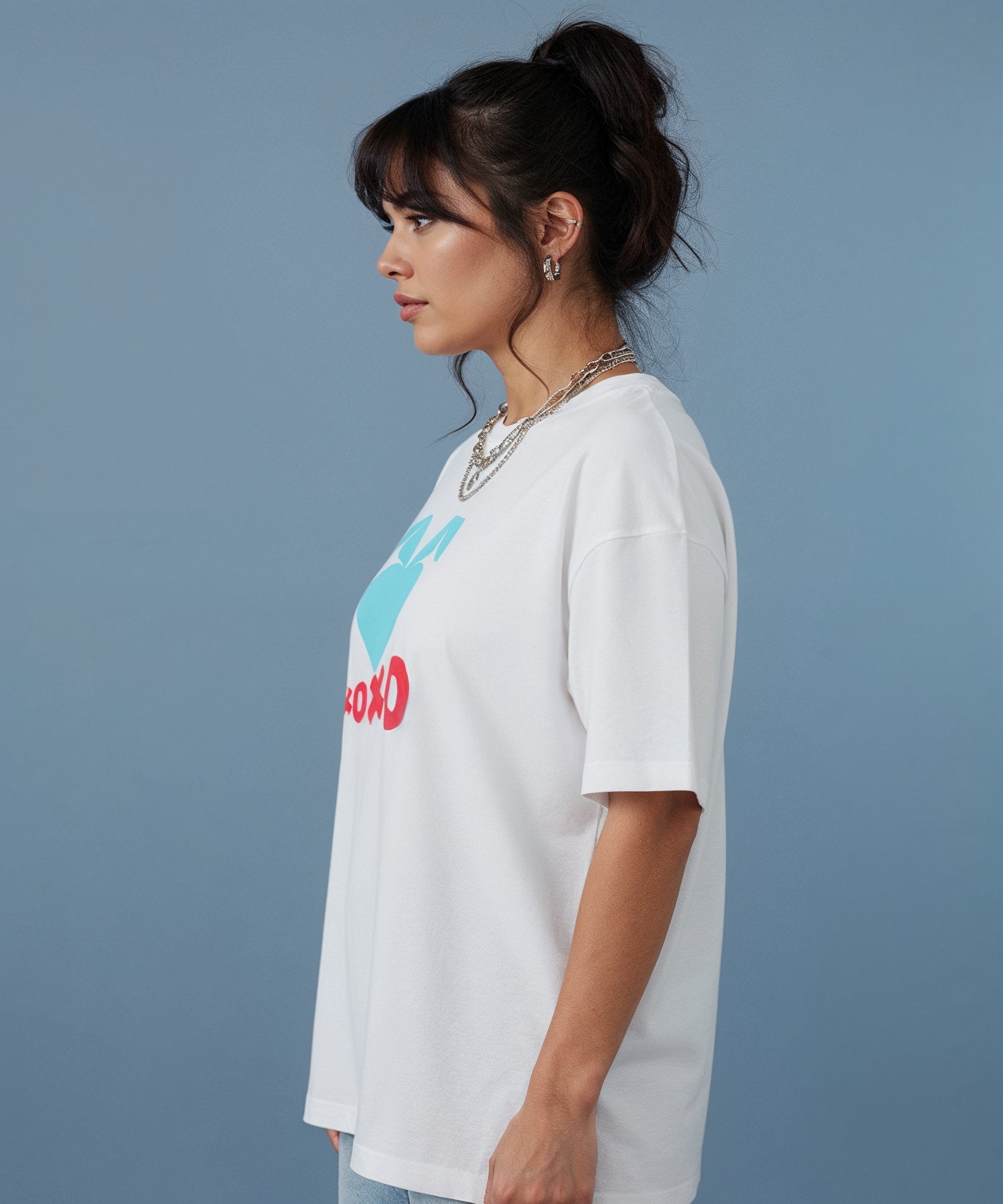 female wearing a white t-shirt with the sweethearts hearts and hugs logo  graphic design on a gray background, side view