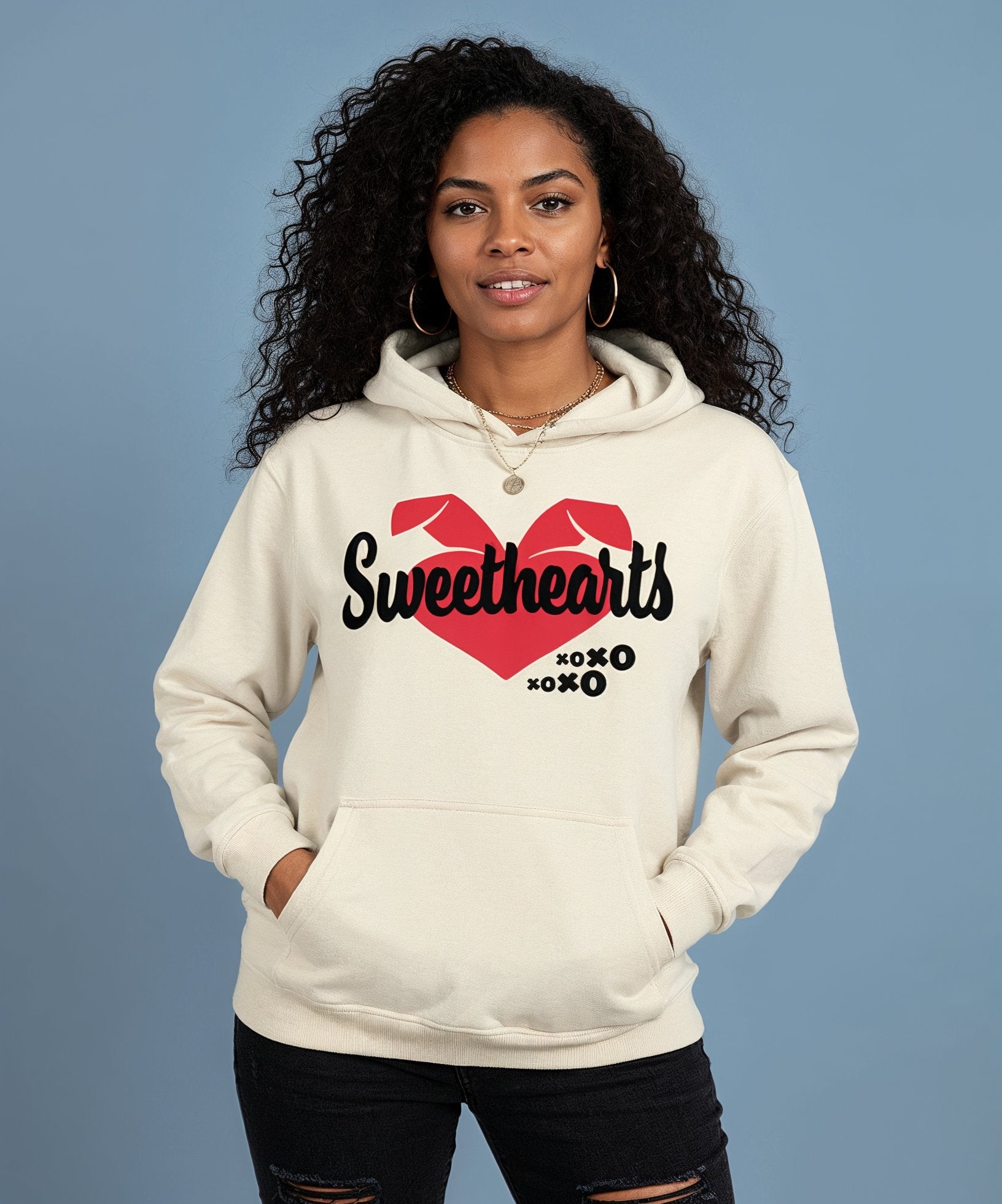 Woman wearing a cream hoodie with 'Sweethearts' design on a blue background