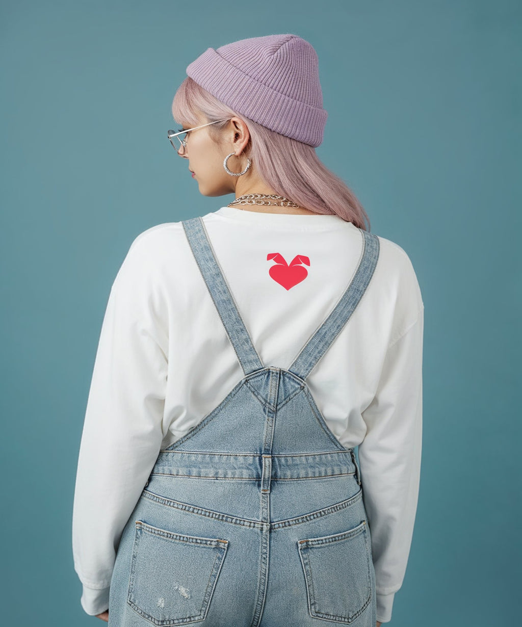 Person wearing a white sweatshirt with a red logo and blue denim overalls on a teal background