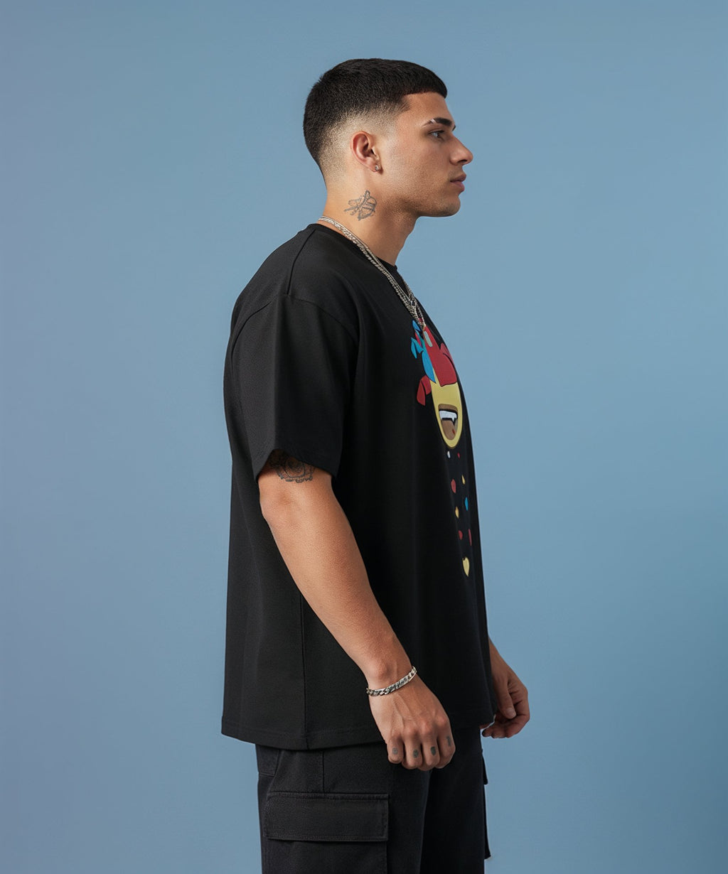 Man wearing a black t-shirt with a colorful sweethearts emoji design on a blue background, side view