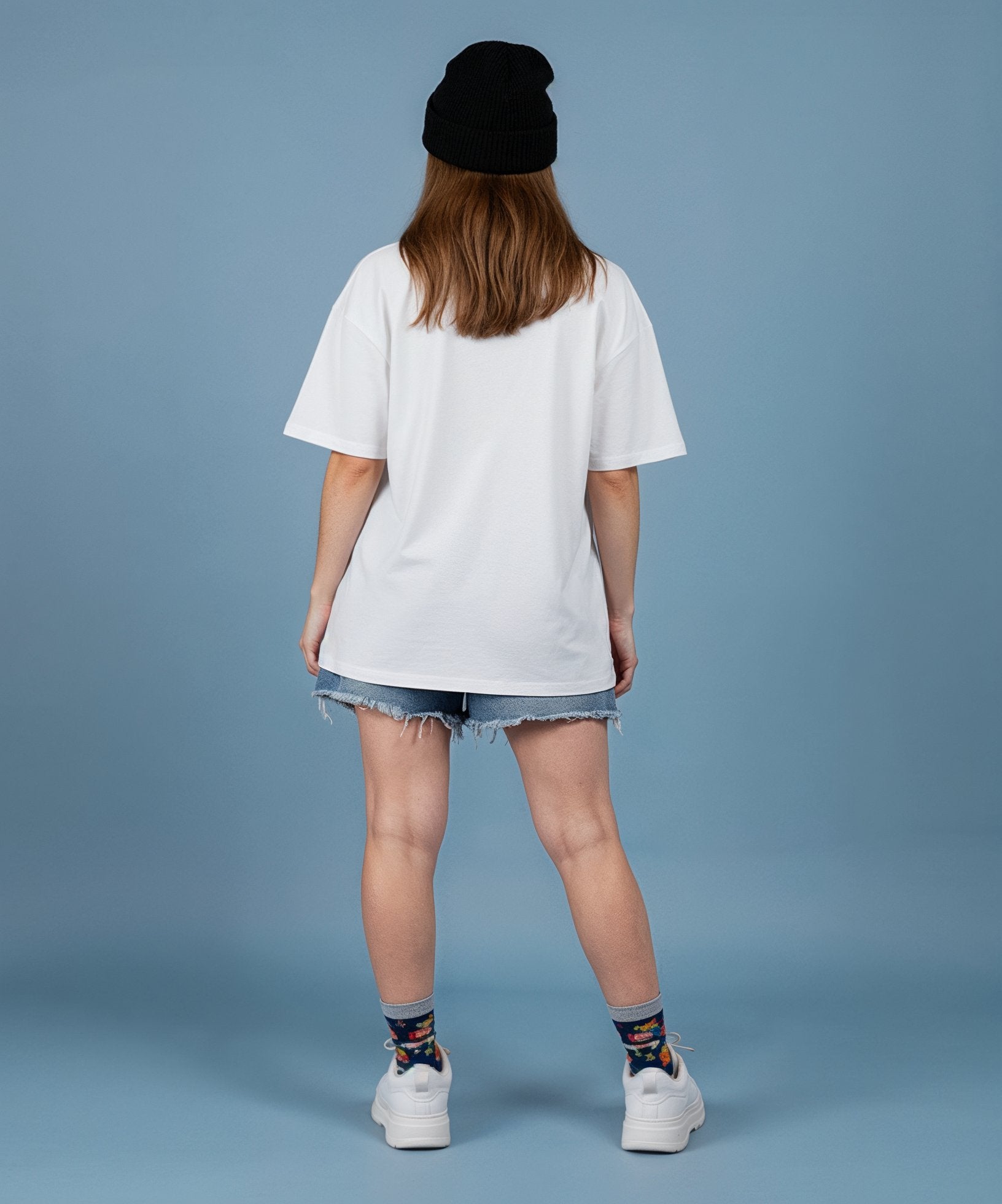 female wearing a sweethearts white t-shirt with a colorful graphic design and ripped jeans on a blue background. back view
