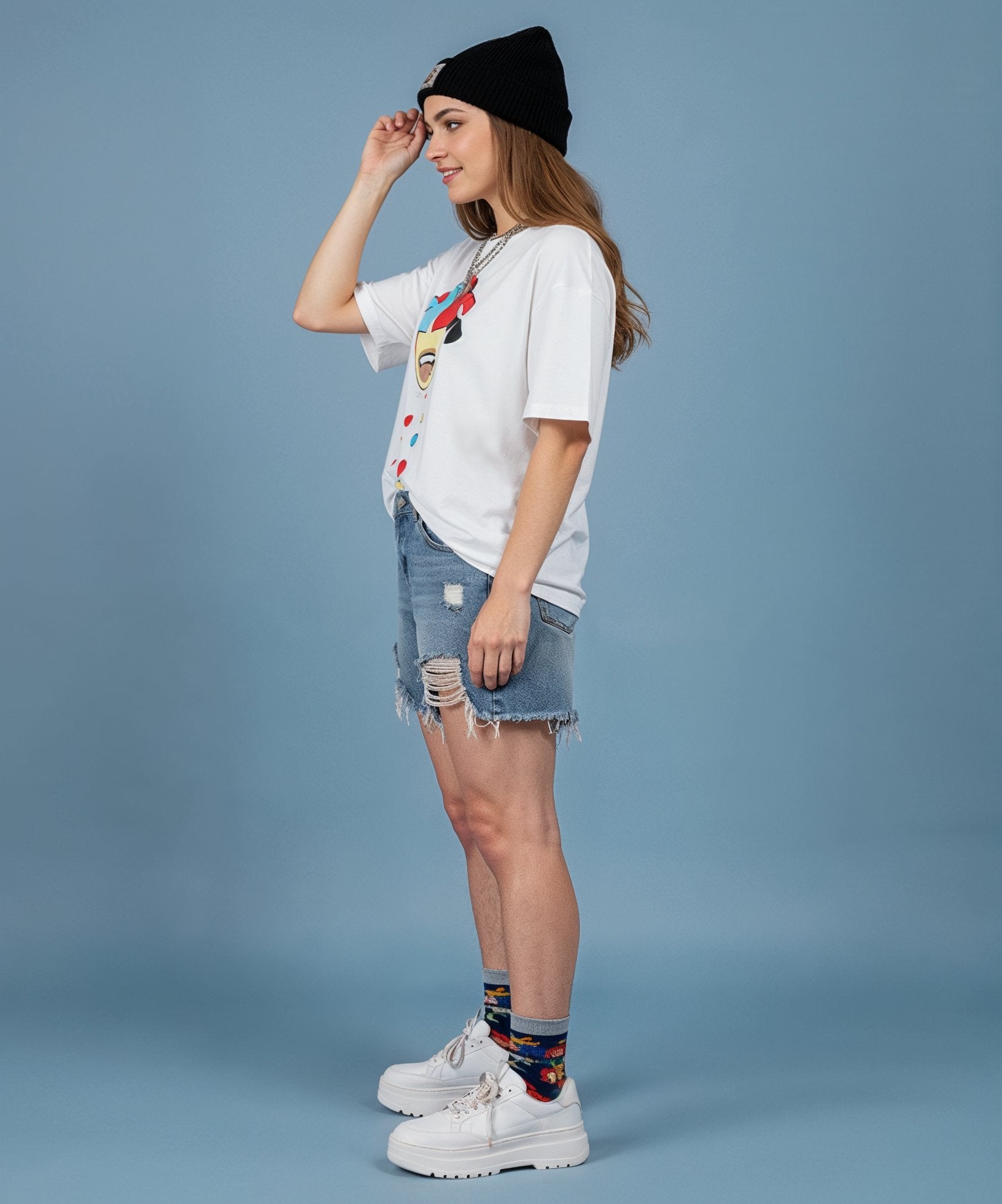 female wearing a sweethearts white t-shirt with a colorful graphic design and ripped jeans on a blue background. side view
