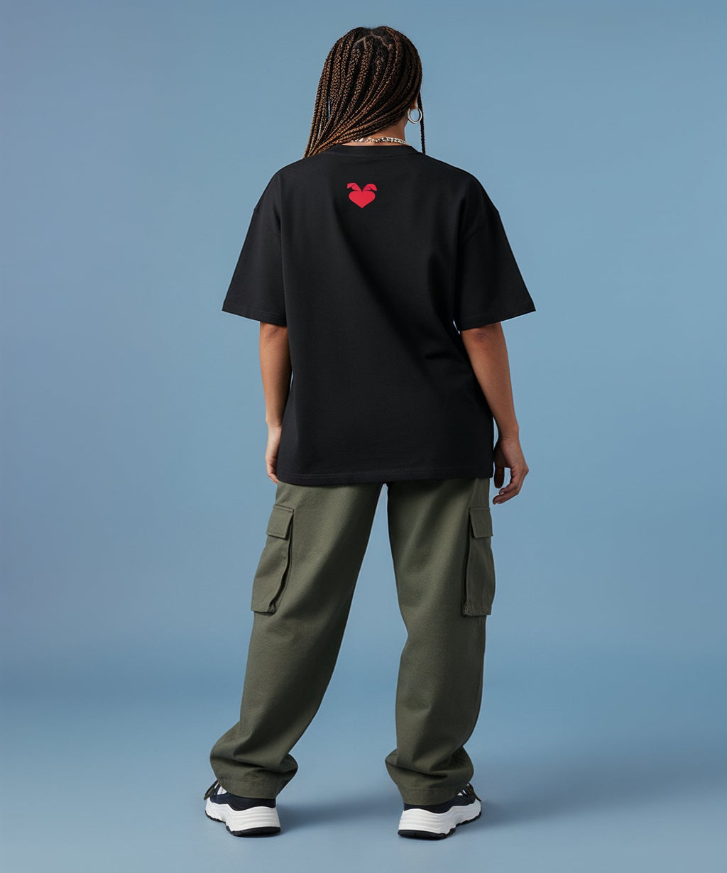 female wearing a black t-shirt with a sweethearts red heart logo on her back and green cargo pants on a blue background
