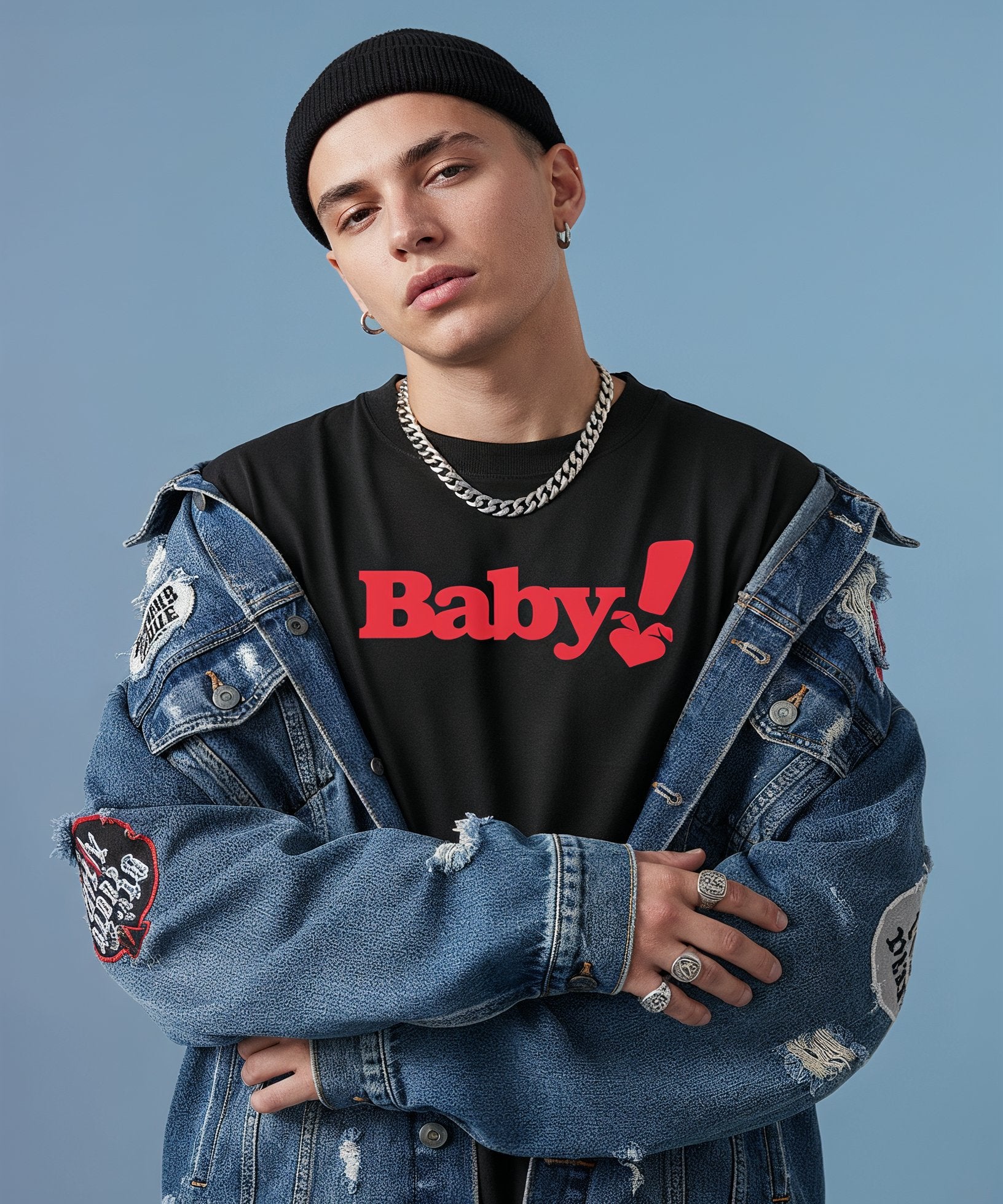 male wearing a denim jacket with patches and a black shirt with sweethearts red "baby" text, standing against a plain background. front view