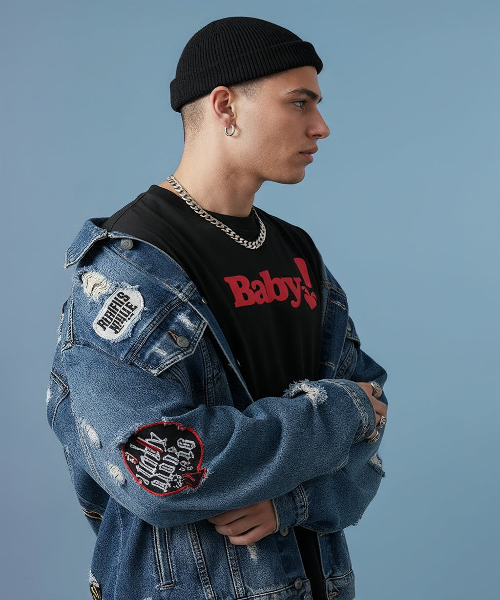 male wearing a denim jacket with patches and a black shirt with sweethearts red "baby" text, standing against a plain background. side view