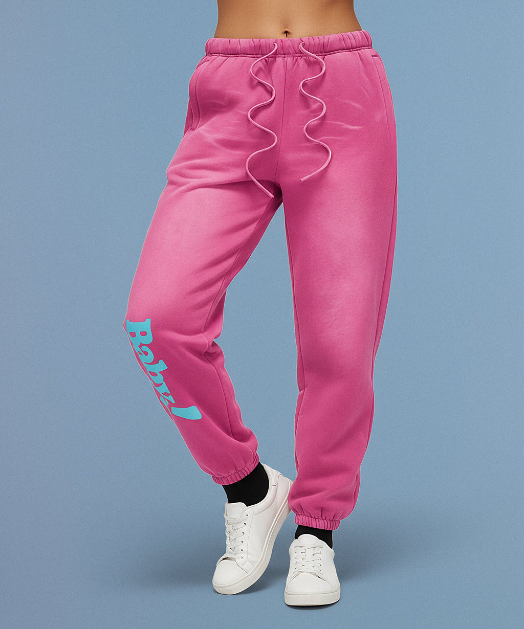 Pink sweatpants with sweethearts  'Baby!' text on a blue background, female front view