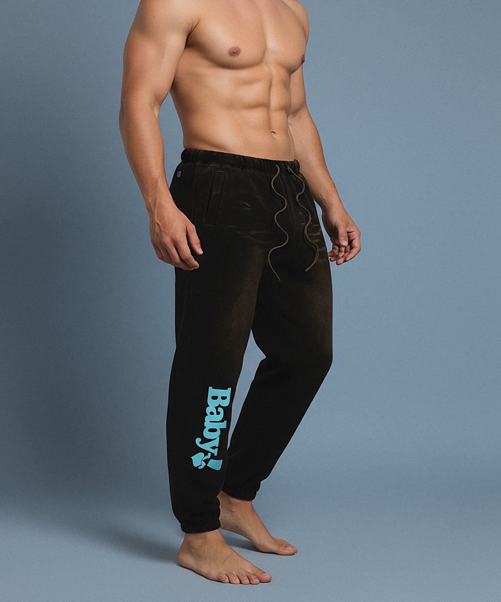 Black sweatpants with sweethearts 'Baby!' text on a gray background, male front side view