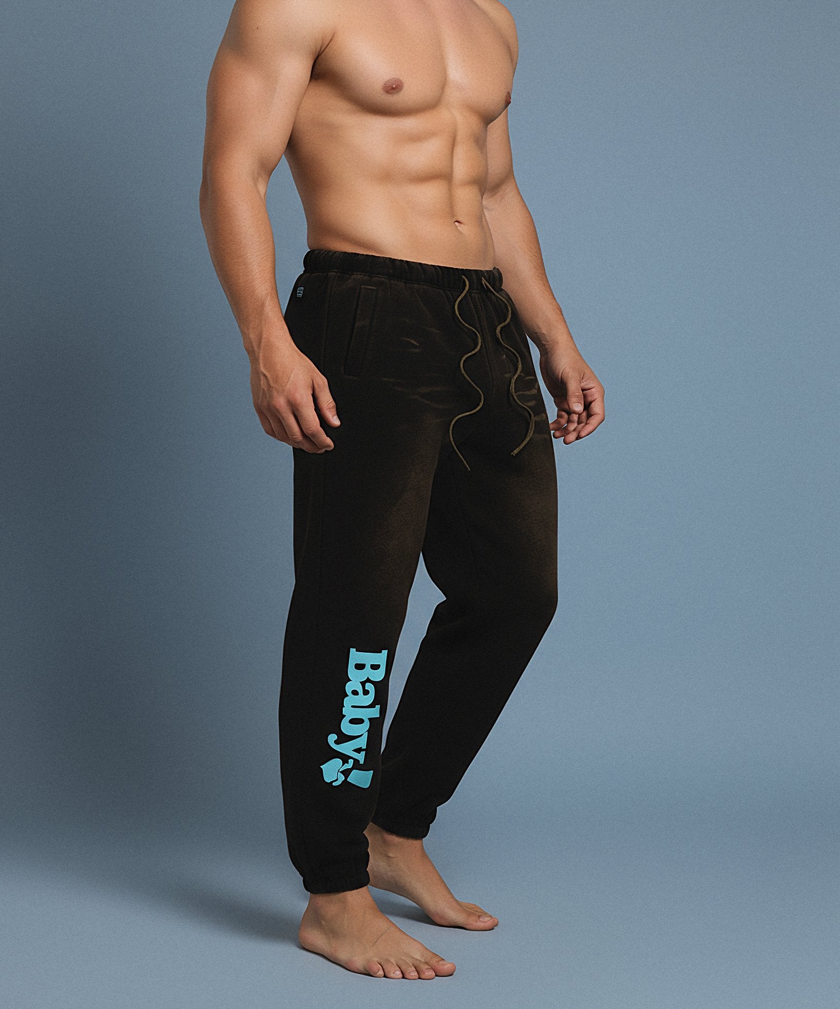Black sweatpants with sweethearts 'Baby!' text on a gray background, male front side view