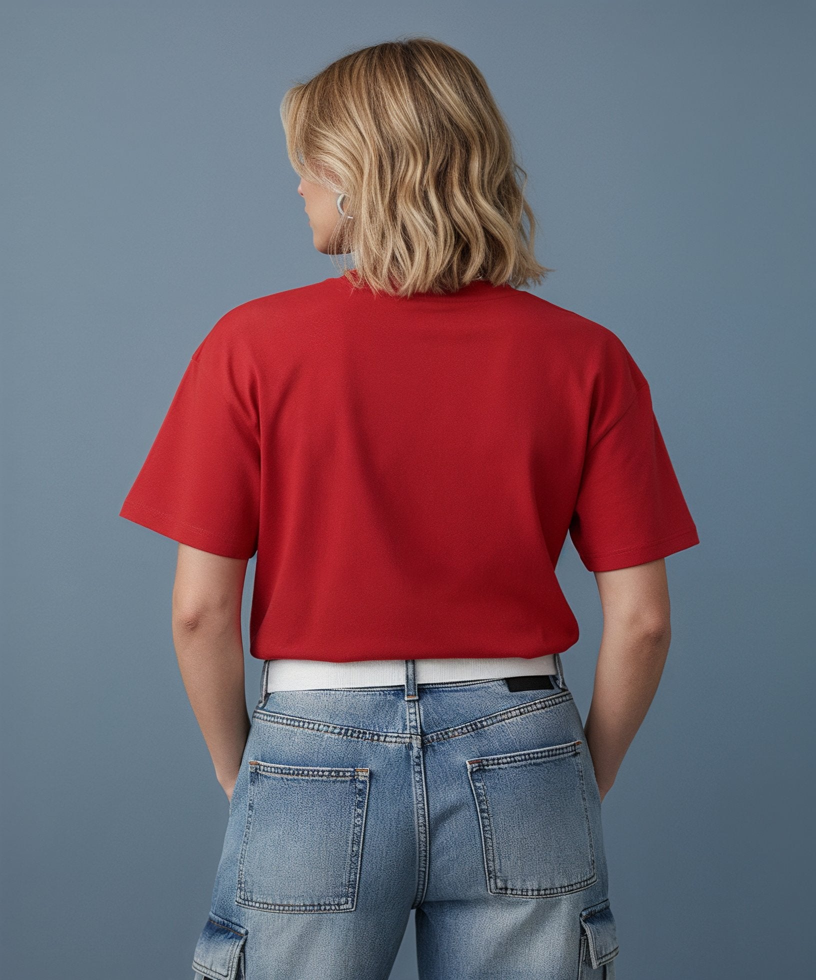 Woman wearing a red t-shirt with baby text and blue jeans on a blue background, back view