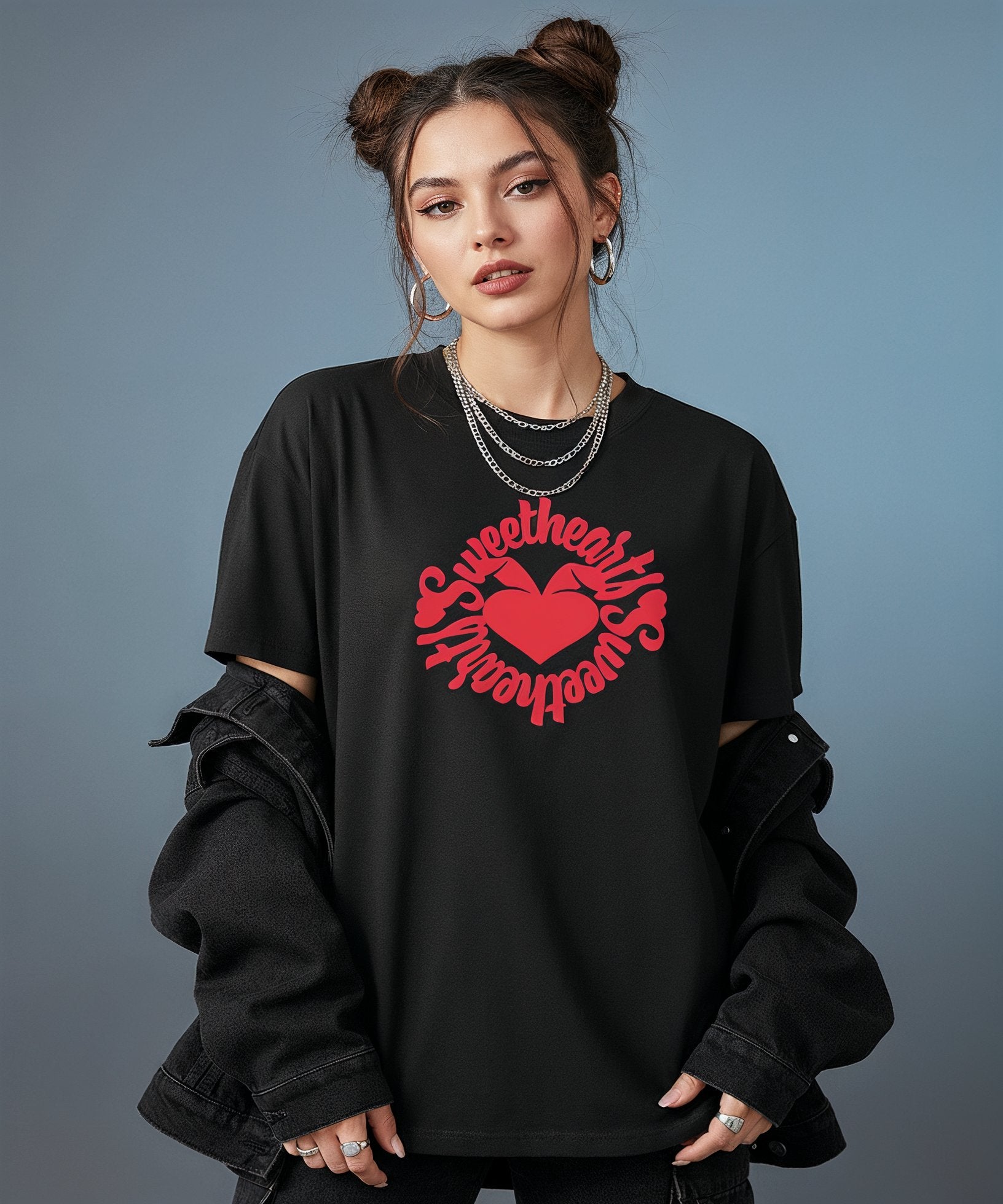 female wearing a black t-shirt with sweethearts red heart logo graphics and text in a circle and distressed jeans on a blue background, front view