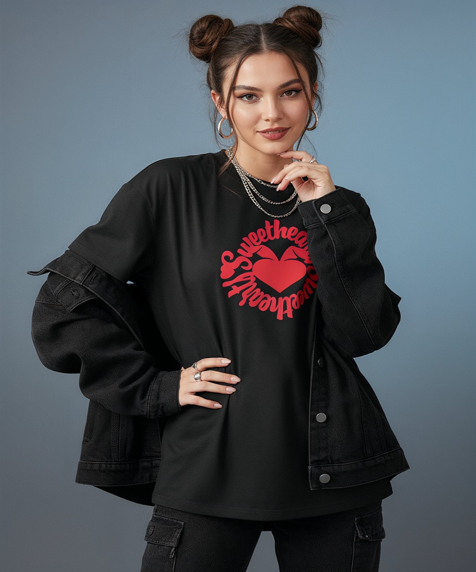 female wearing a black t-shirt with sweethearts red heart logo graphics and text in a circle and distressed jeans on a blue background, front view