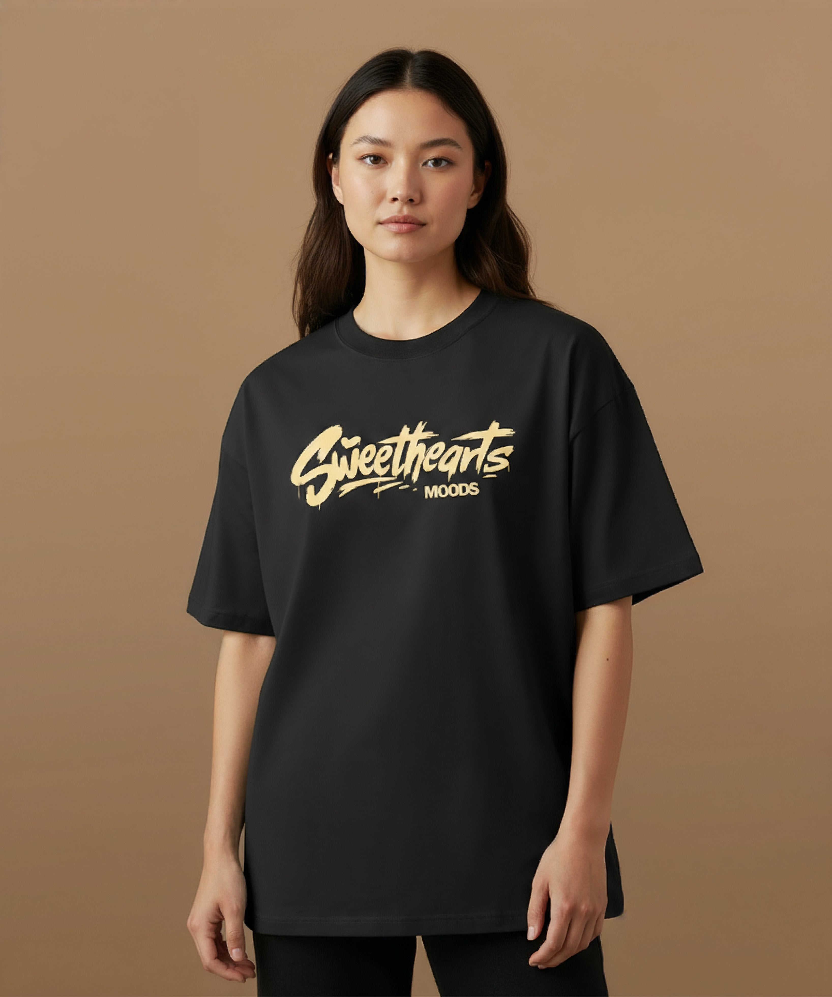Male model wearing a black t-shirt with 'Sweethearts' logo from moods collection,  graffiti text logo, on a brown background, center pose