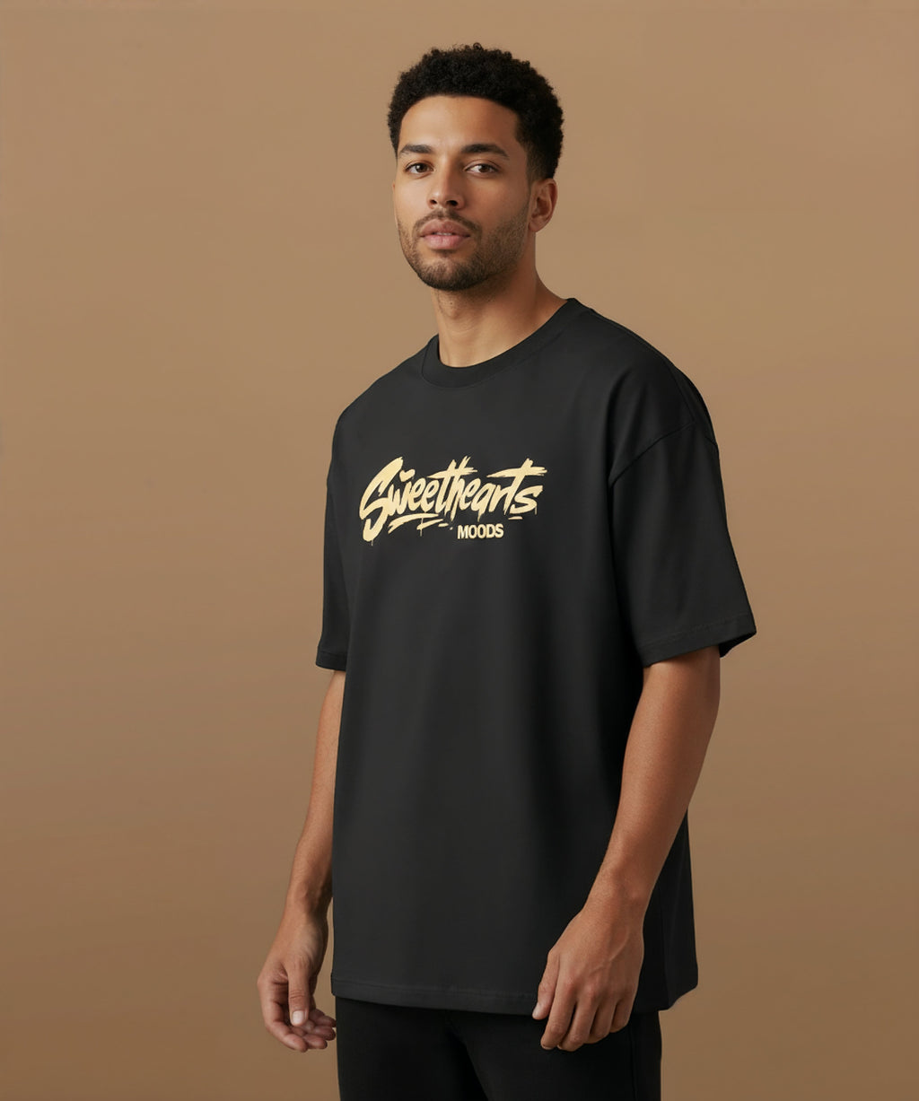 Male model wearing a black t-shirt with 'Sweethearts' logo from moods collection,  graffiti text logo, on a brown background, angled left