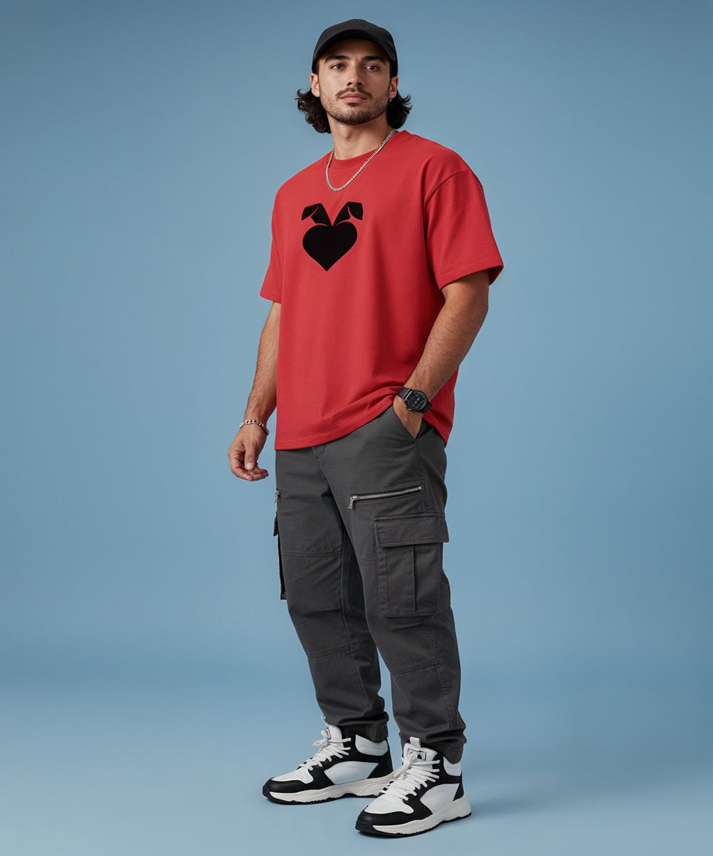 Man wearing a red t-shirt with a sweethearts logo, gray cargo pants, and black and white sneakers on a blue background