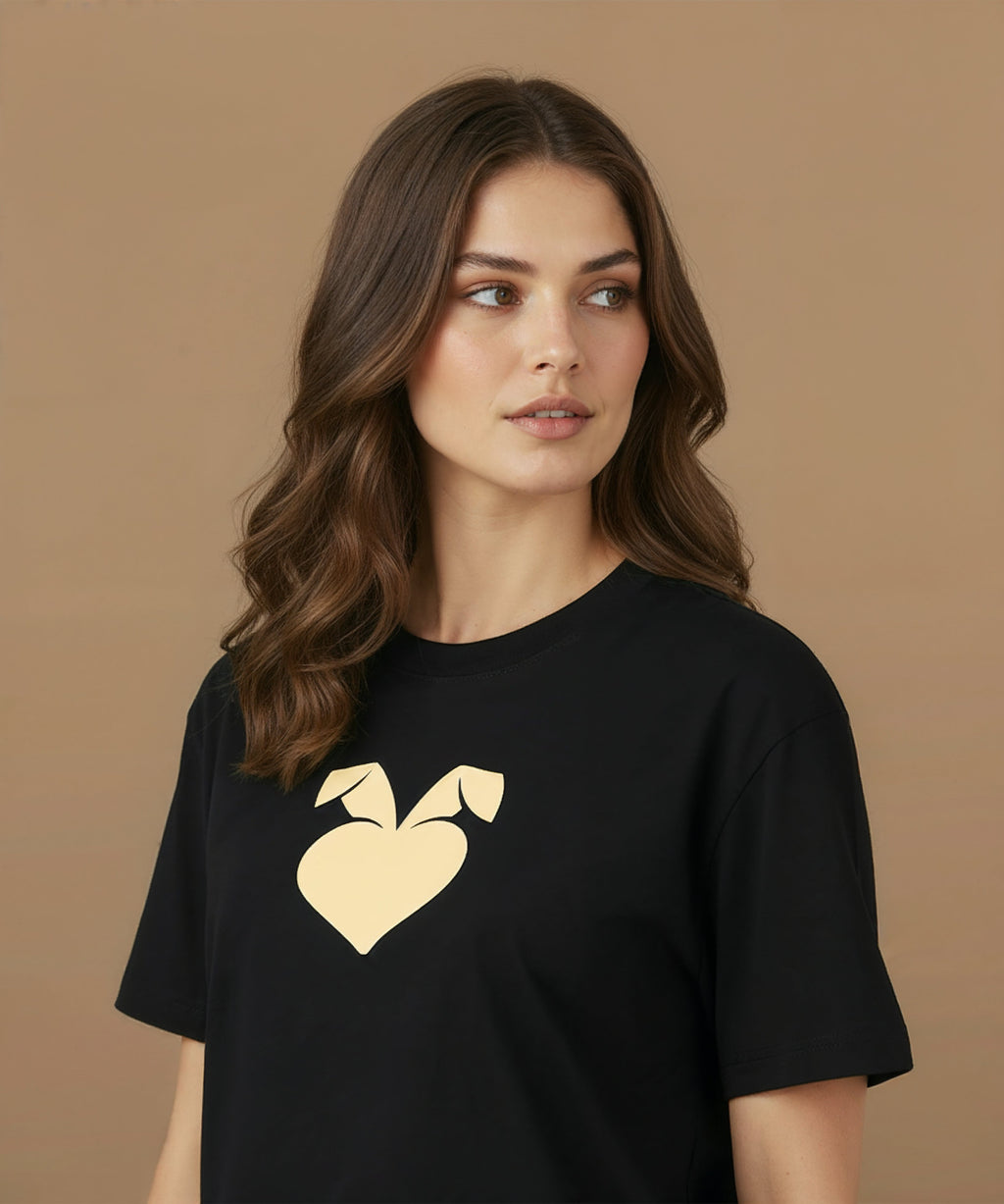 a female wearing a black sweethearts mood edition logo t-shirt with a gold heart design on a brown background, angled left