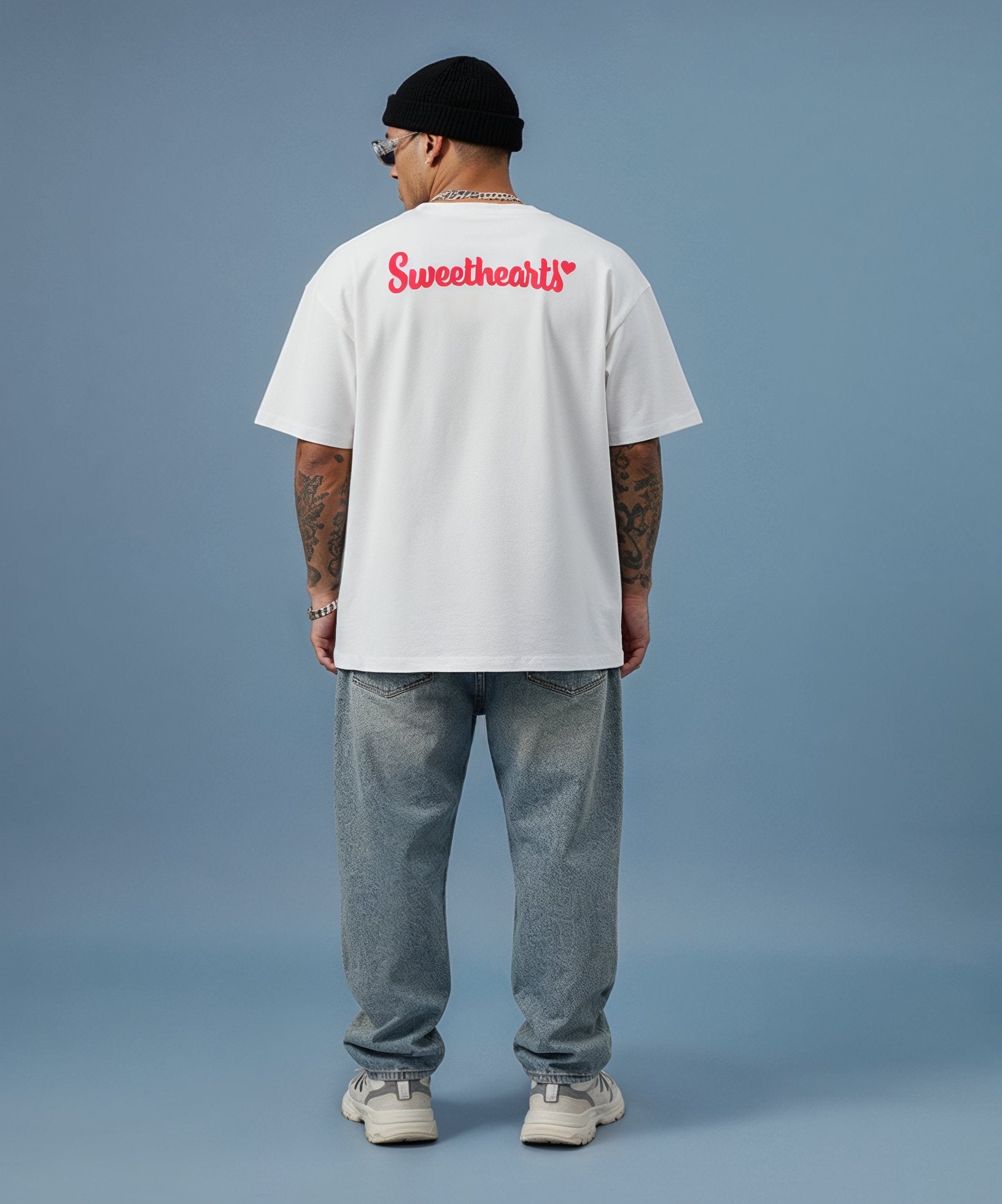 male model wearing white t-shirt with a red sweethearts logo text design on a blue background, back view