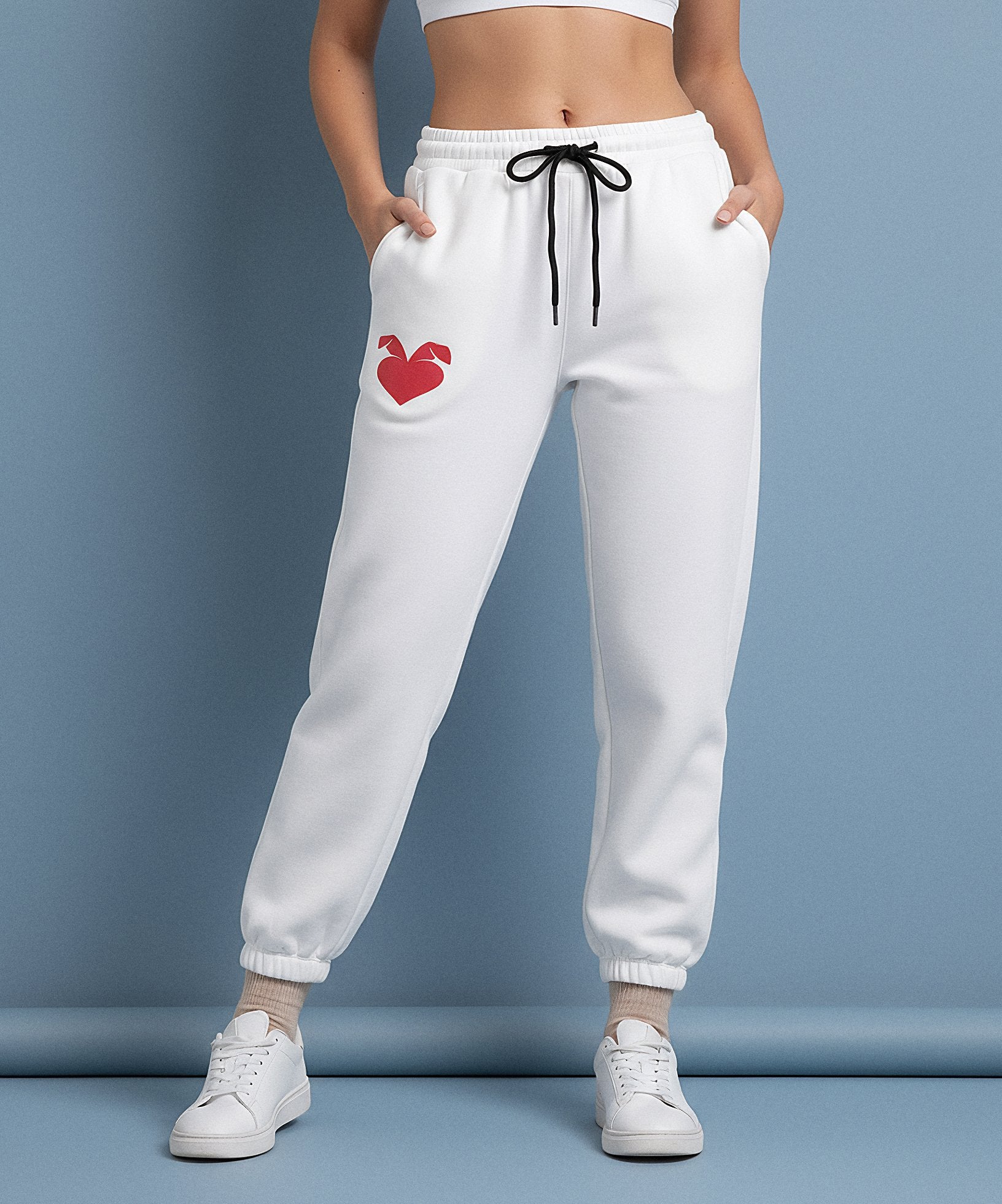 female wearing white sweatpants with a sweethearts red heart logo design on a blue background, front view