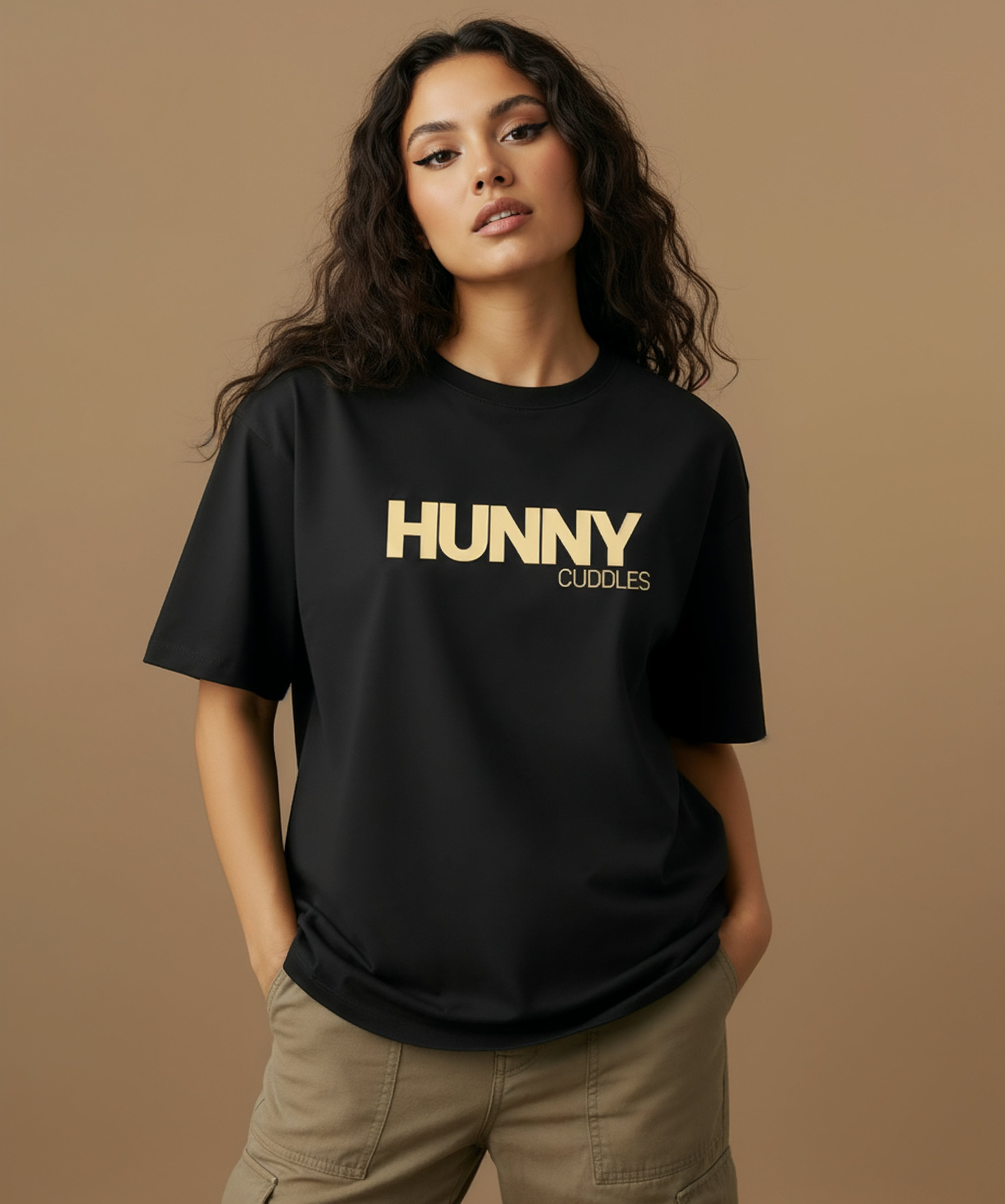 female model wearing a black t-shirt with 'HUNNY CUDDLES' text on a beige background, medium close up.