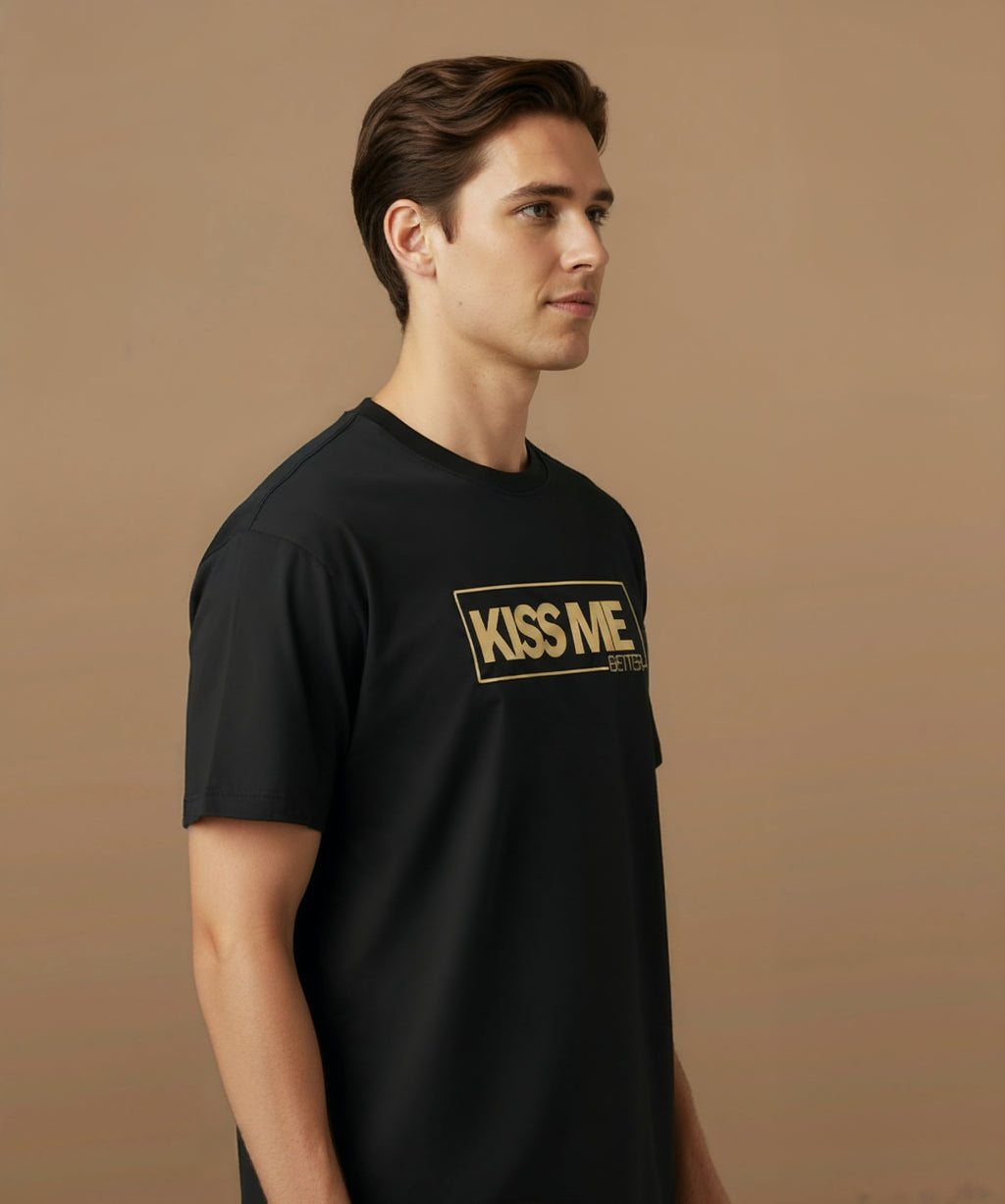 a male wearing a black t-shirt with 'KISS ME BETTER' text on a brown background, angled right