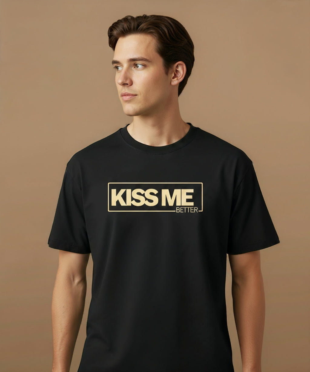 a male wearing a black t-shirt with 'KISS ME BETTER' text on a brown background