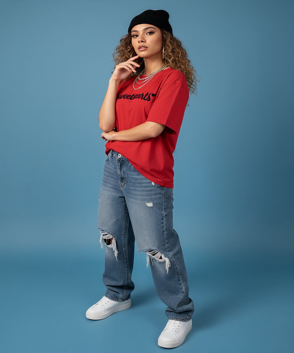 female wearing a red 'Sweetheart' shirt, blue jeans, and white sneakers on a blue background, side view