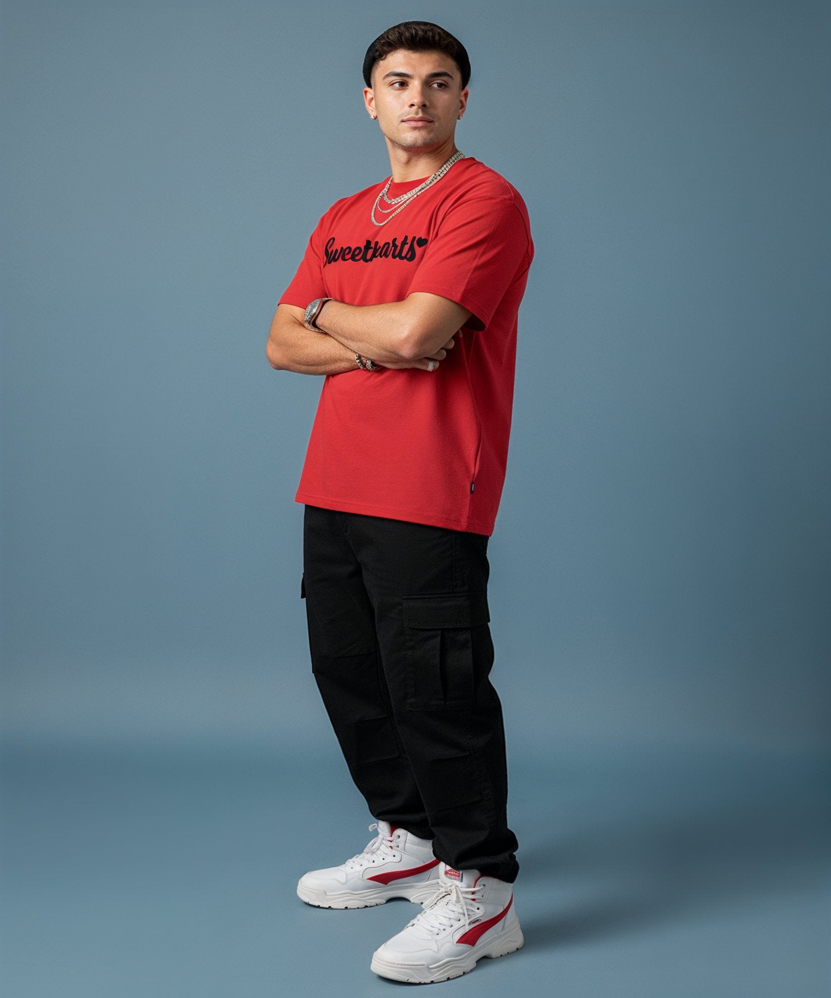 male wearing a red 'Sweetheart' shirt, blue jeans, and white sneakers on a blue background, side view