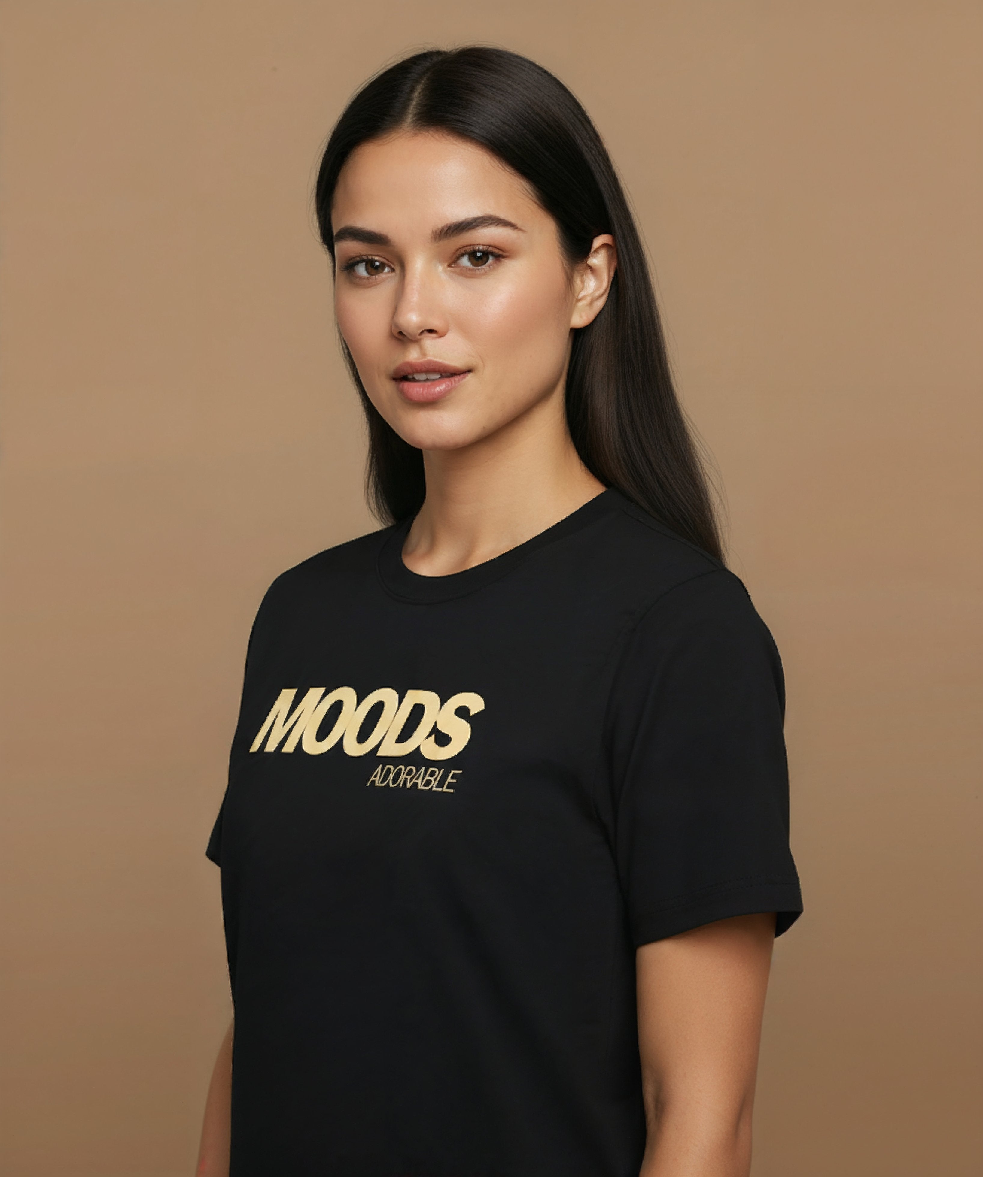 A female wearing a black t-shirt with 'MOODS', adorable, printed in gold on a brown background, angled left