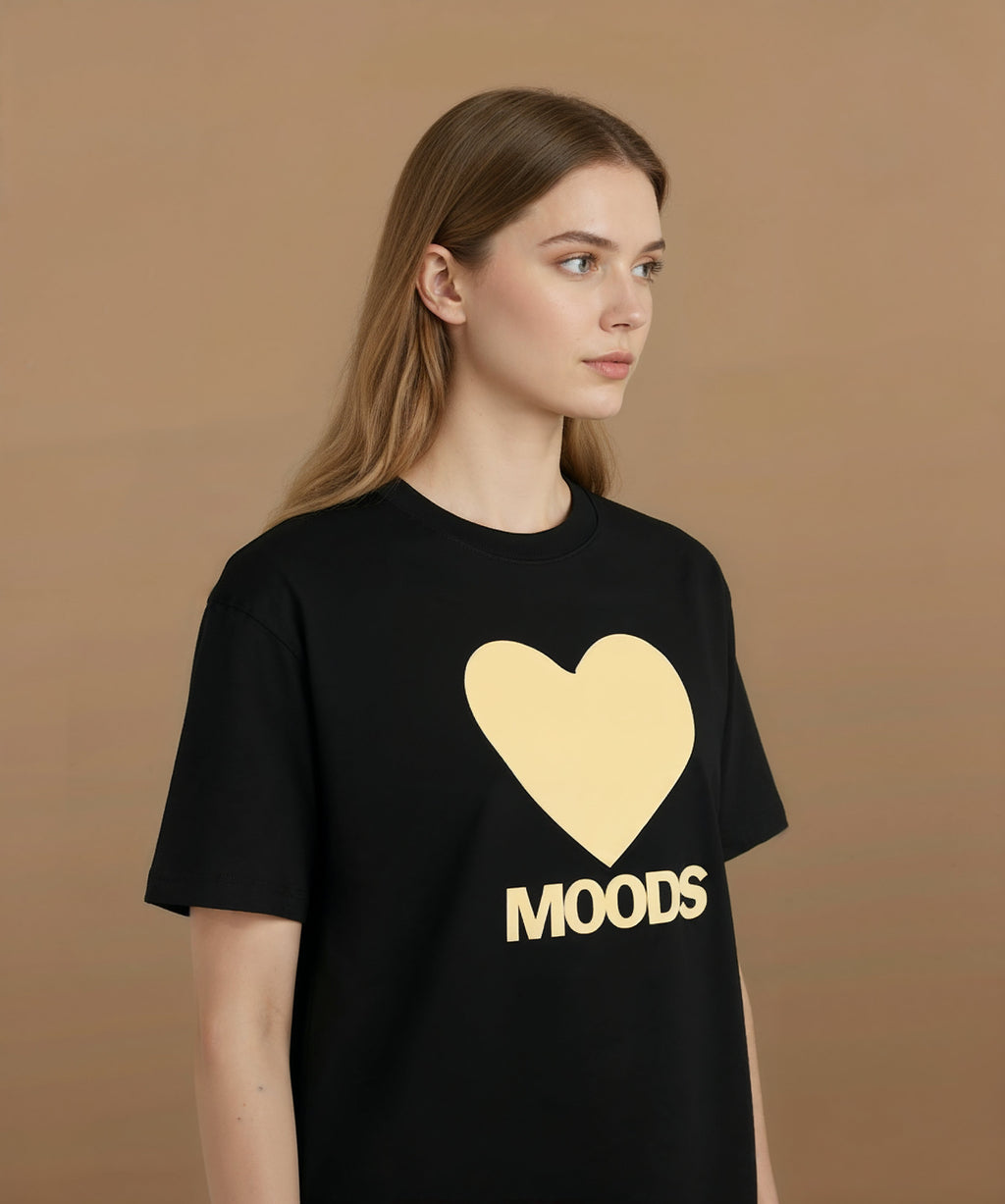 Female angled left wearing a black sweethearts t-shirt with a gold heart and 'MOODS' text on a brown background