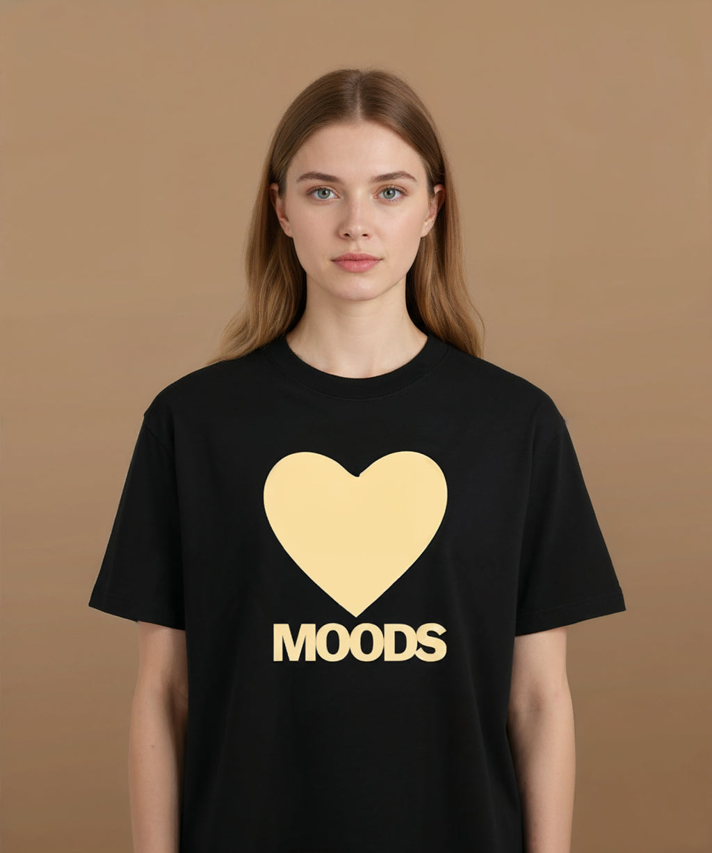 Female wearing a black sweethearts t-shirt with a gold heart and 'MOODS' text on a brown background