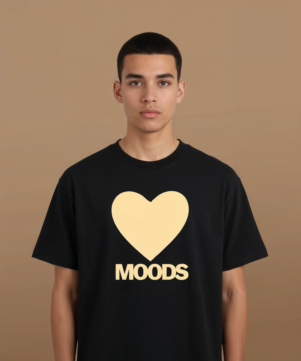 a male wearing a black sweethearts t-shirt with a gold heart and 'MOODS' text on a brown background
