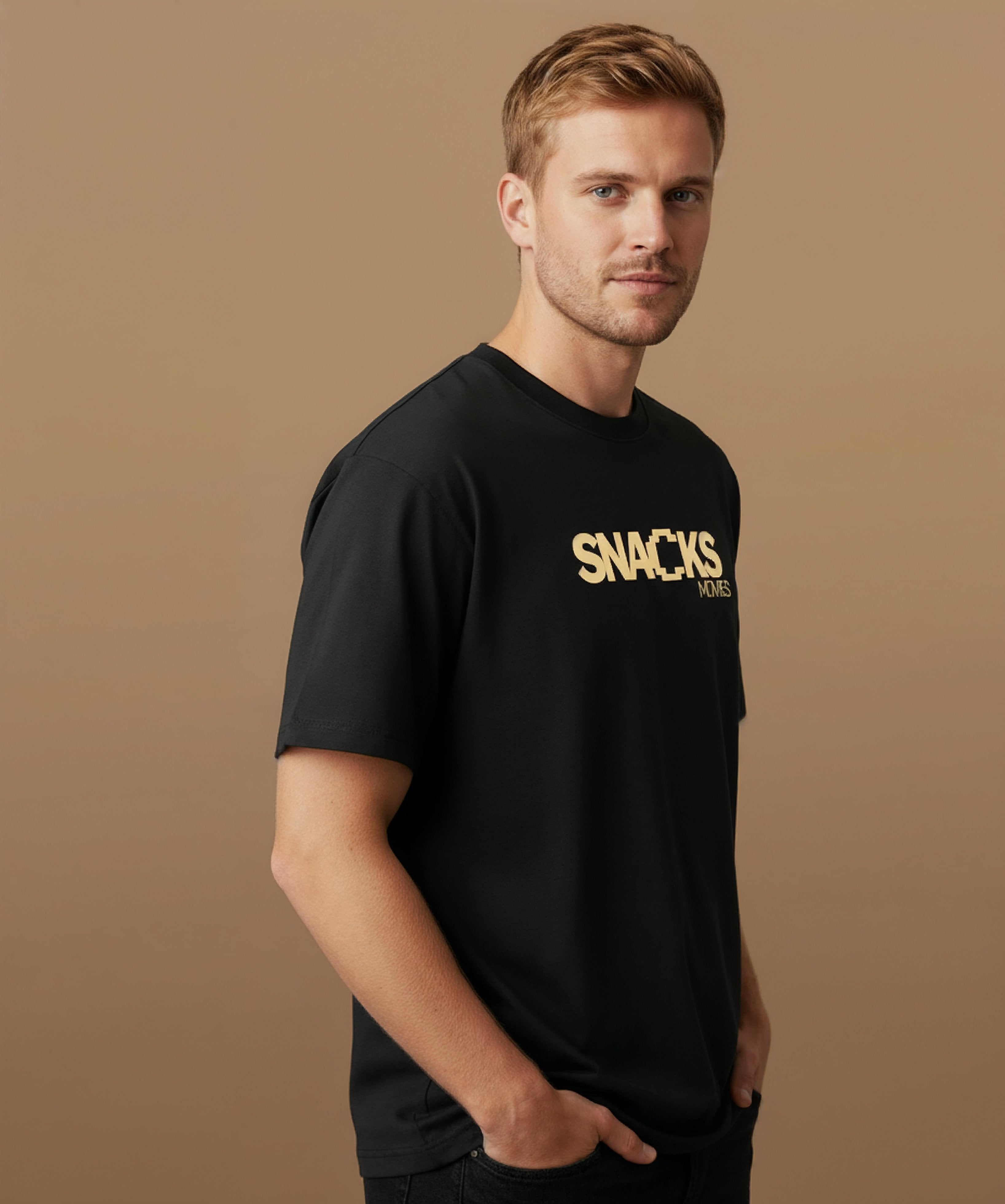 Male model wearing a black t-shirt with sweethearts brand 'SNACKS' printed in yellow from moods collection on a brown background. he is angled right