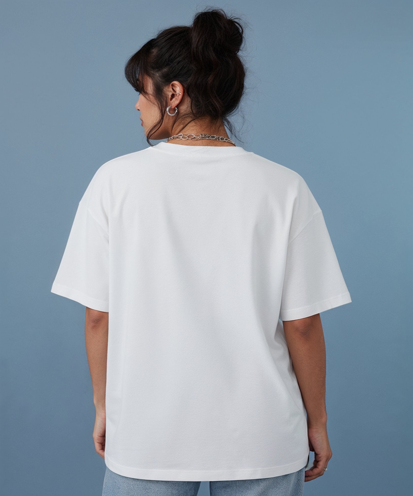 female wearing a white t-shirt with the sweethearts hearts and hugs logo  graphic design on a gray background, back view