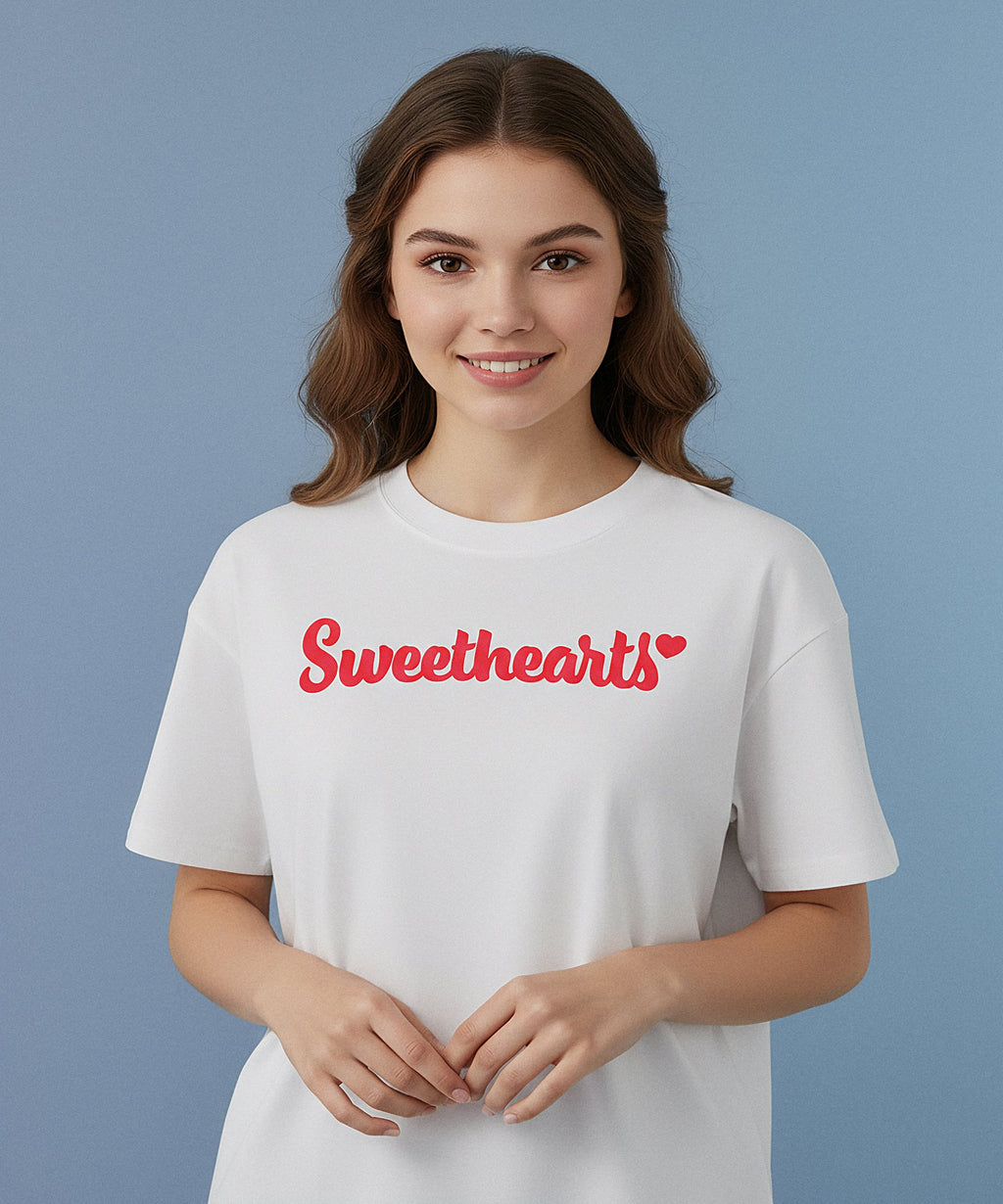 female wearing a white t-shirt with sweethearts in red text design on the front of her shirt, a blue background, front view