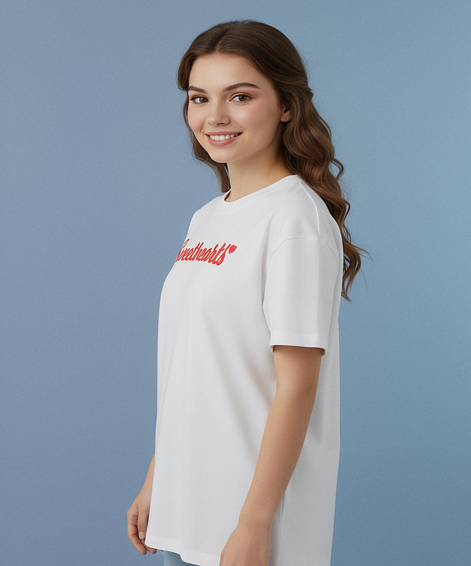 female wearing a white t-shirt with sweethearts in red text design on the front of her shirt, a blue background, side view