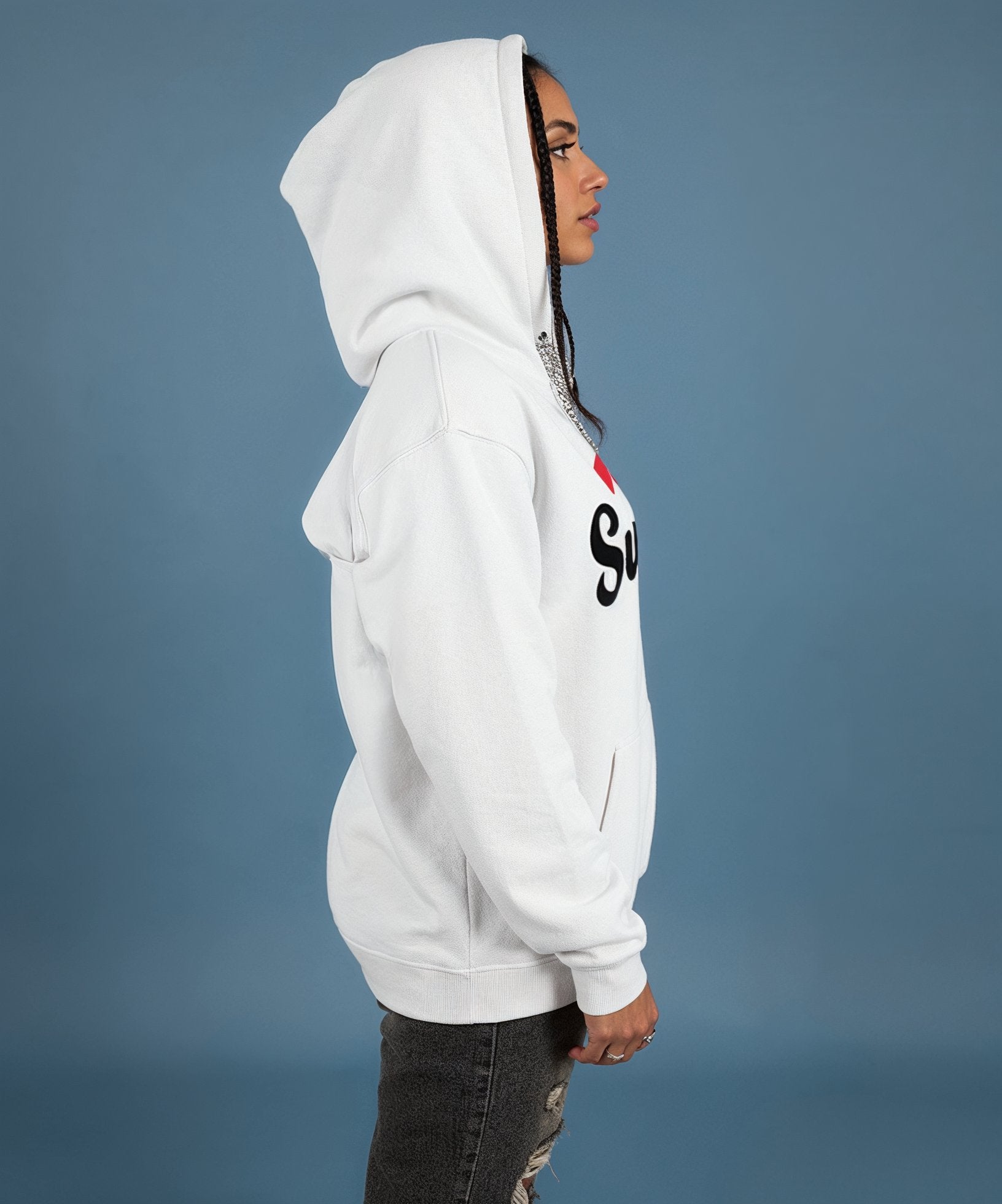 female wearing a white hoodie with a sweethearts red heart logo and xoxo design and text on a blue background, side view